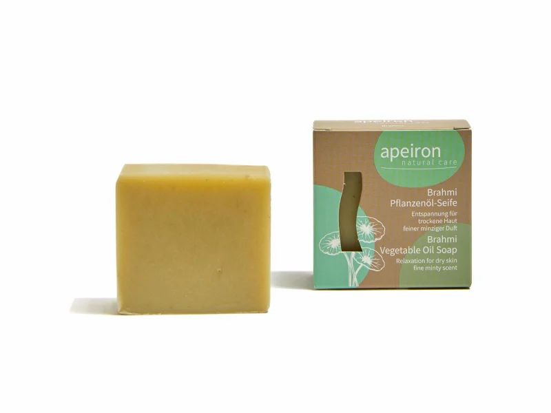 Quadratische Seife und Verpackung. Seife hellgelb, Verpackung braun mit grünem Aufdruck. Text: apeiron, Brahmi Pflanzenöl-Seife, Vegetable Oil Soap.