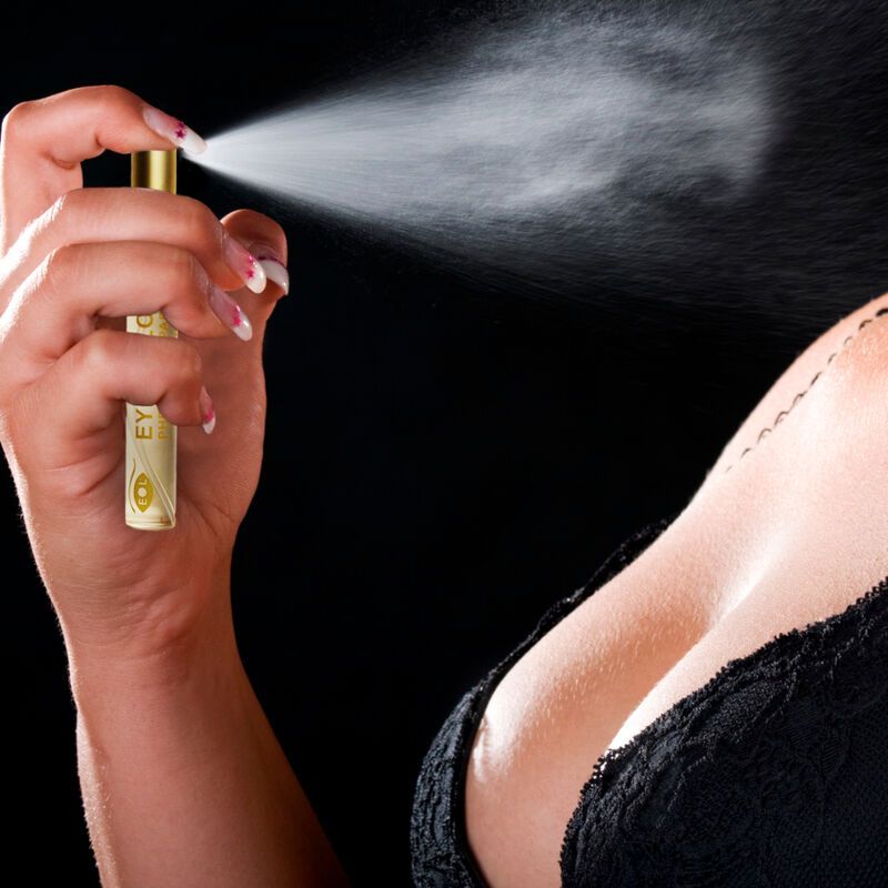 Person sprüht Parfum. Sichtbar: Flasche mit Aufschrift Eye of Love, Dekolleté, Fingernägel. Schwarzer Hintergrund.