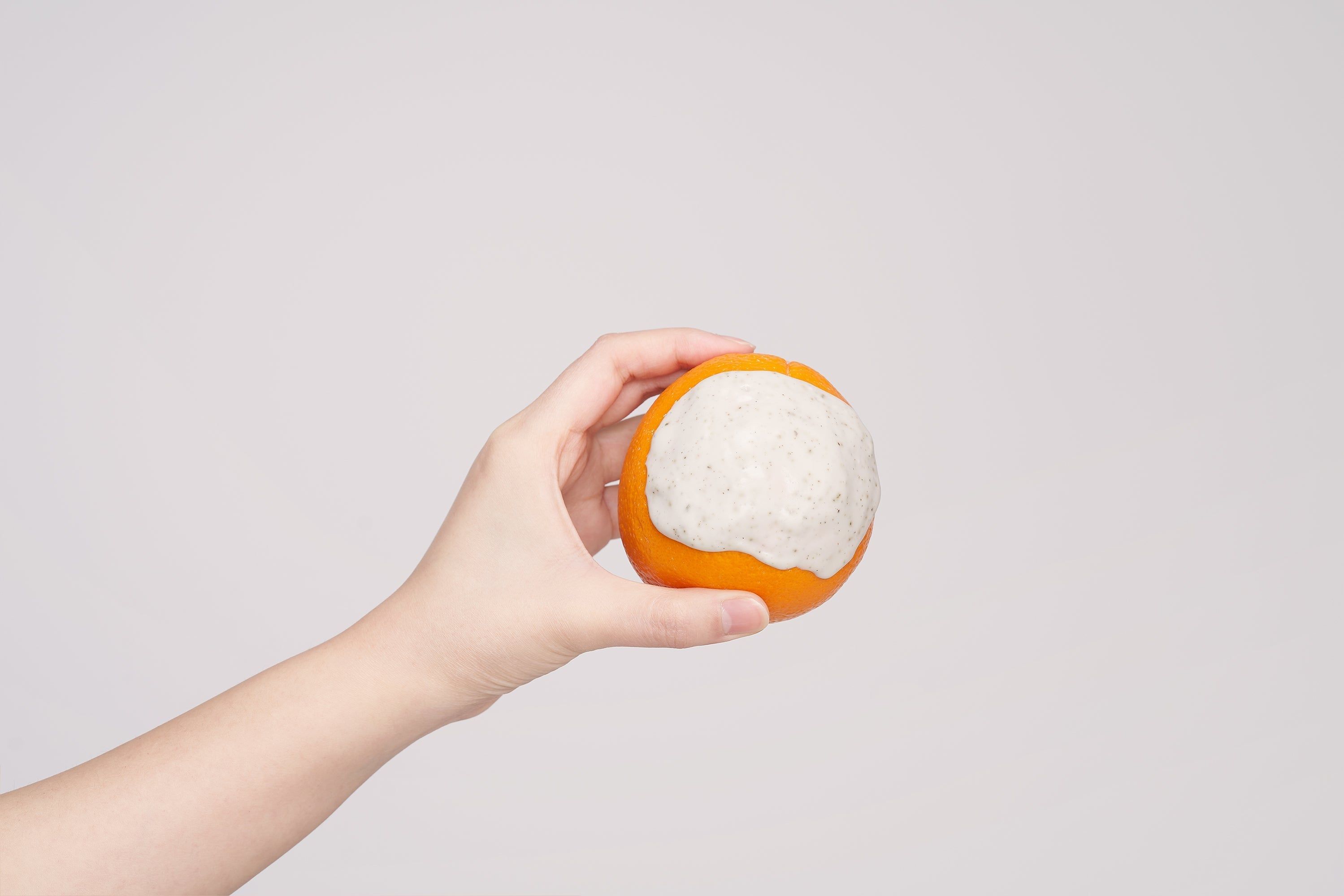 Hand hält eine orangefarbene Kugel, bedeckt mit weißem Material. Auf weißem Hintergrund.