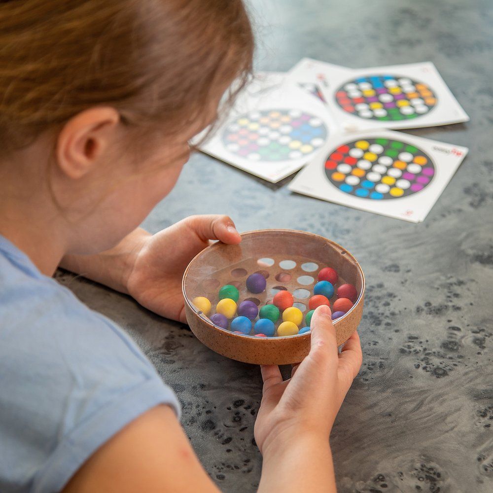 Kind hält ein Spiel mit bunten Kugeln und Karten. Das Spiel hat eine runde Form mit Löchern und einer transparenten Abdeckung.