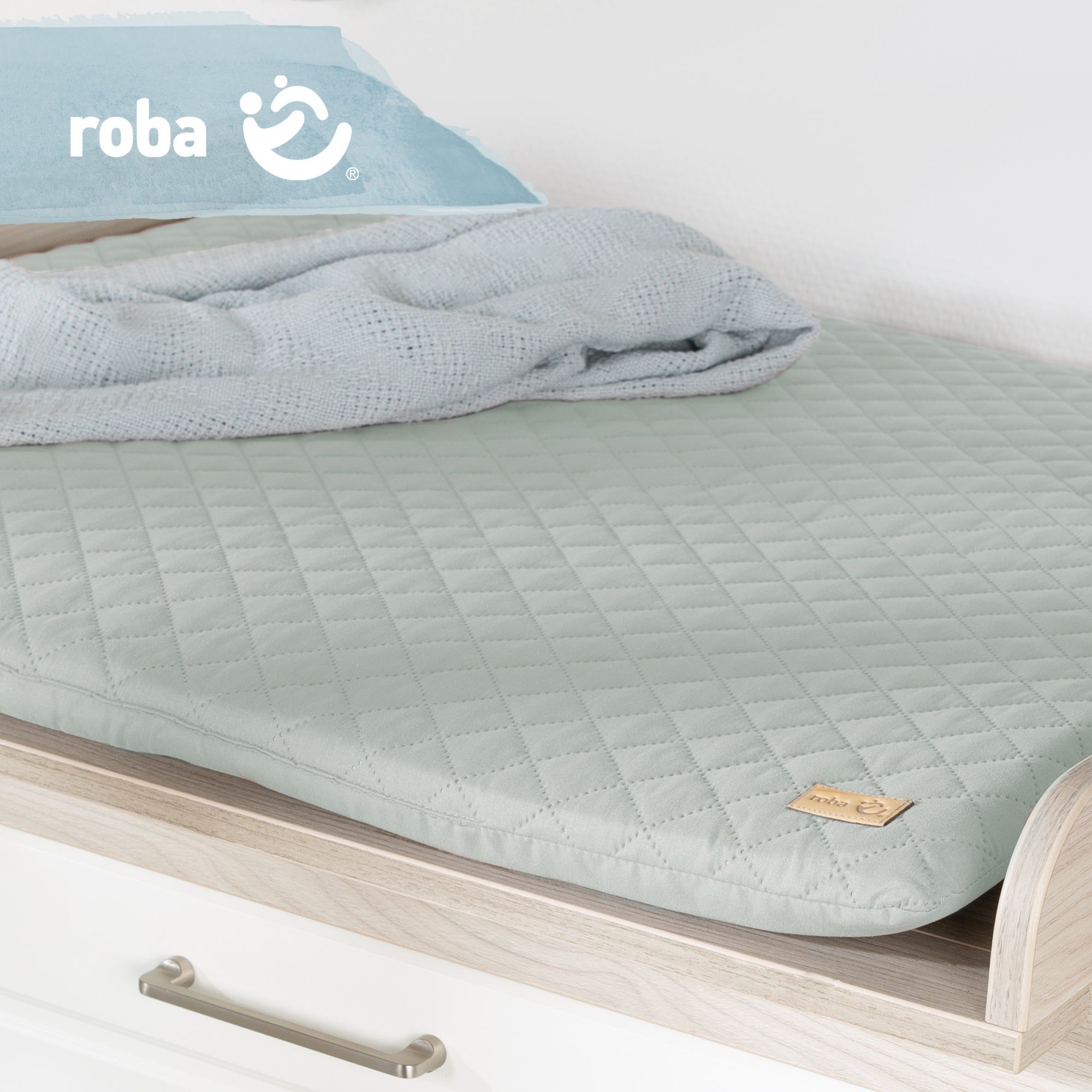 Wickelauflage auf Wickeltisch. Hellgrüne, gesteppte Auflage. Logo 'roba' sichtbar. Decke liegt auf.