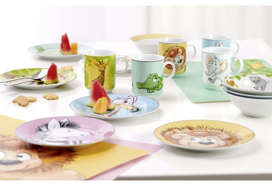 Happy Zoo Geschirr-Set mit Tellern, Bechern und Schüsseln. Verschiedene Tiermotive. Wassermelone und Kekse auf dem Tisch.