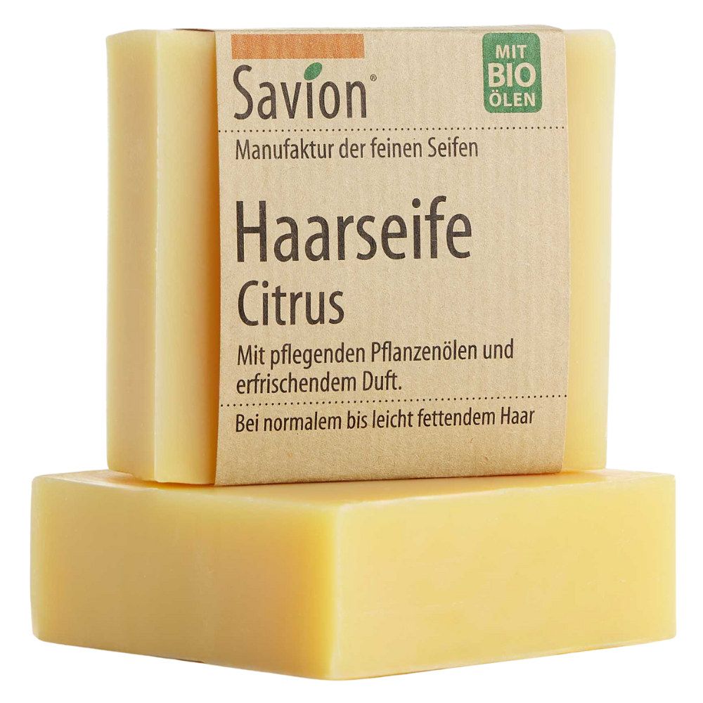 Zwei gelbe Seifenstücke. Das obere hat eine Papierbanderole mit Produktinformationen: Haarseife Citrus, Savion.