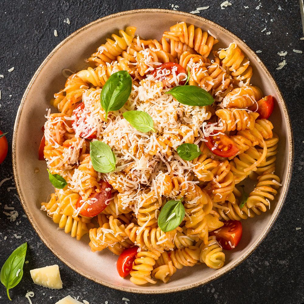Fusilli-Nudeln mit Tomaten, Sauce, Käse und Basilikum in einer Schüssel. Käseflocken und Tomatenstücke.