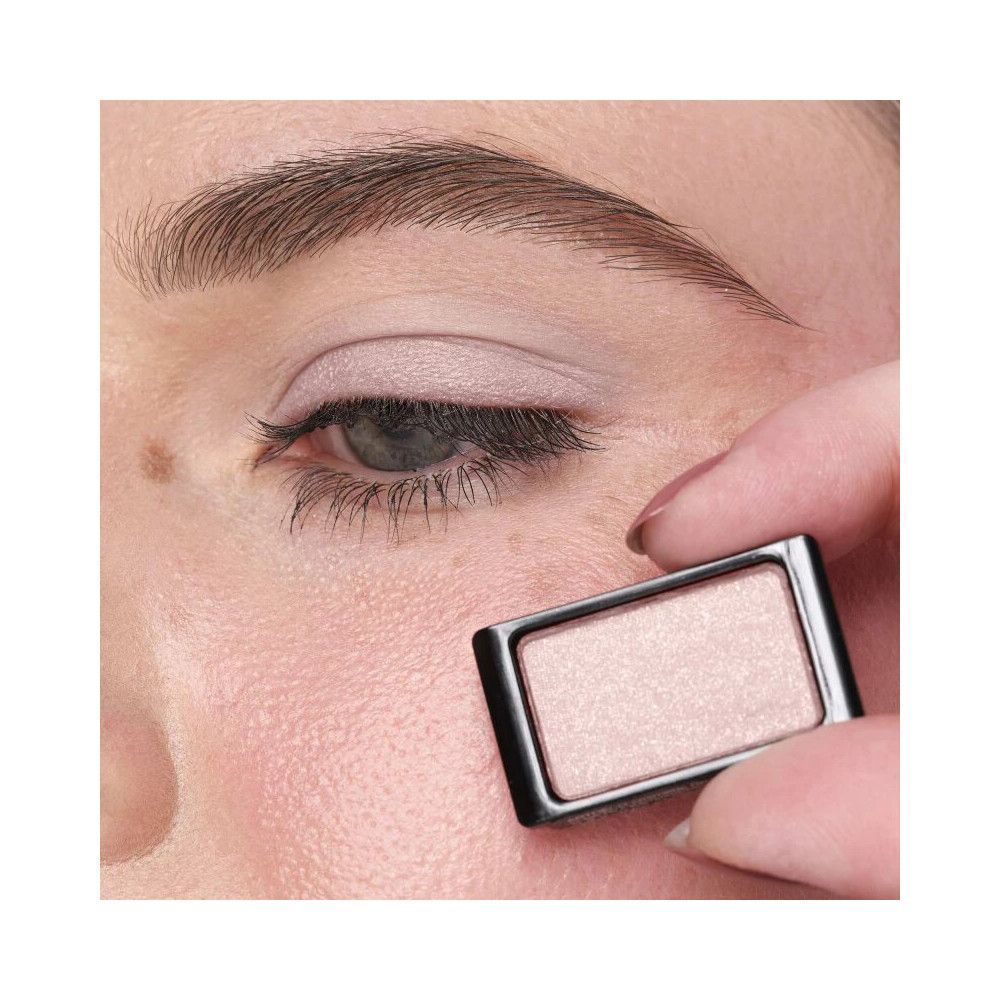 Auge mit aufgetragenem Lidschatten. Eine Hand hält einen Lidschattenbehälter in der Nähe des Auges.