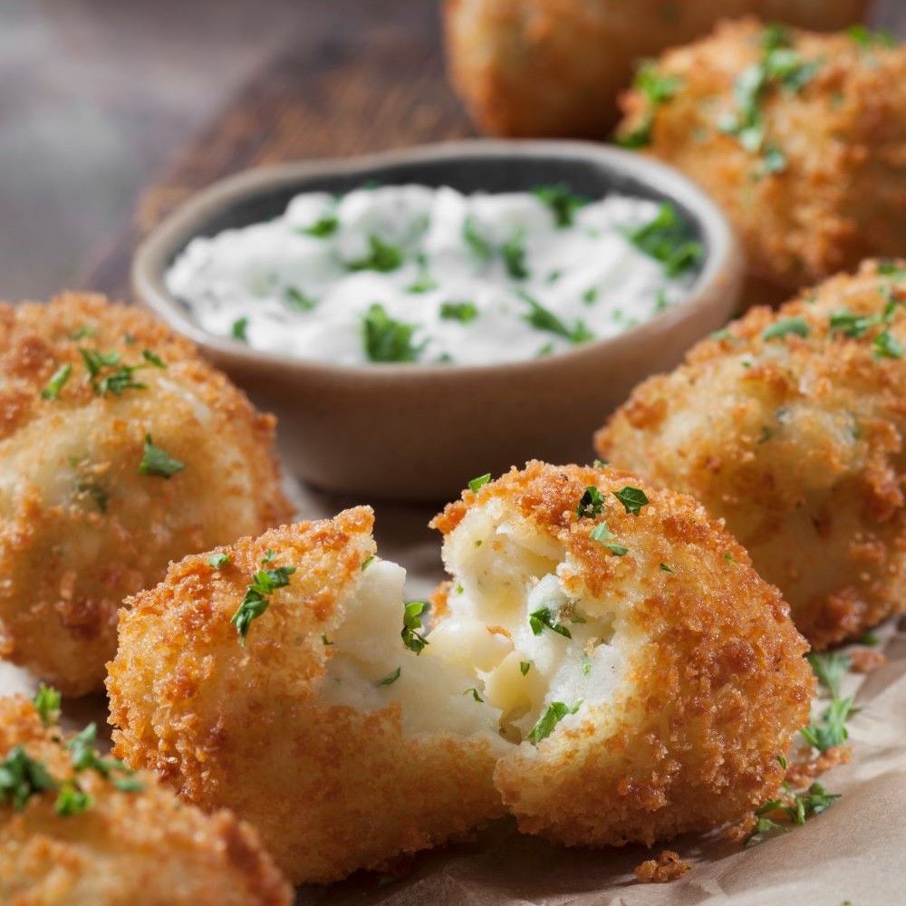 Frittierte Kartoffelkroketten, aufgeschnitten, mit Dip. Kroketten goldbraun, Dip in Schale. Petersilie als Garnitur.