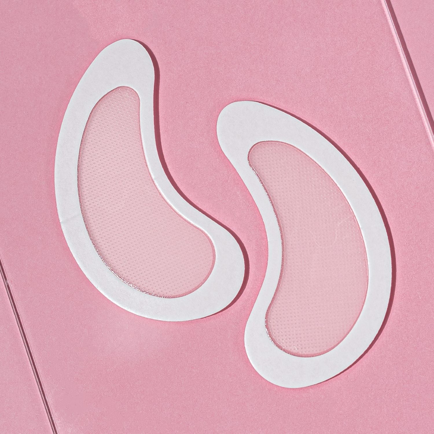 Zwei weiße, augenförmige Pads mit Netzstruktur auf rosa Hintergrund. Pads sind für die Augenpartie bestimmt.