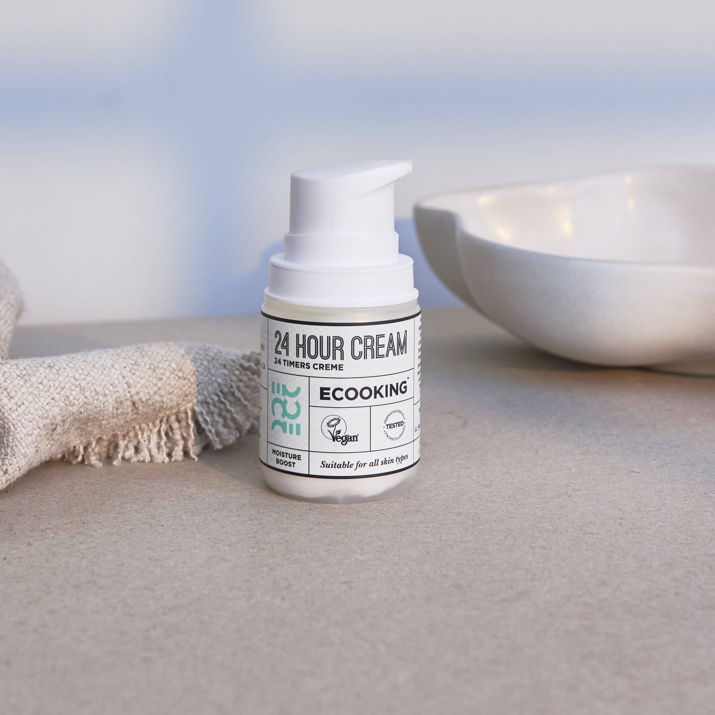 Creme-Spender mit weißem Pumpkopf. Aufschrift: 24 HOUR CREAM, Ecooking. Neben einem Waschbecken.