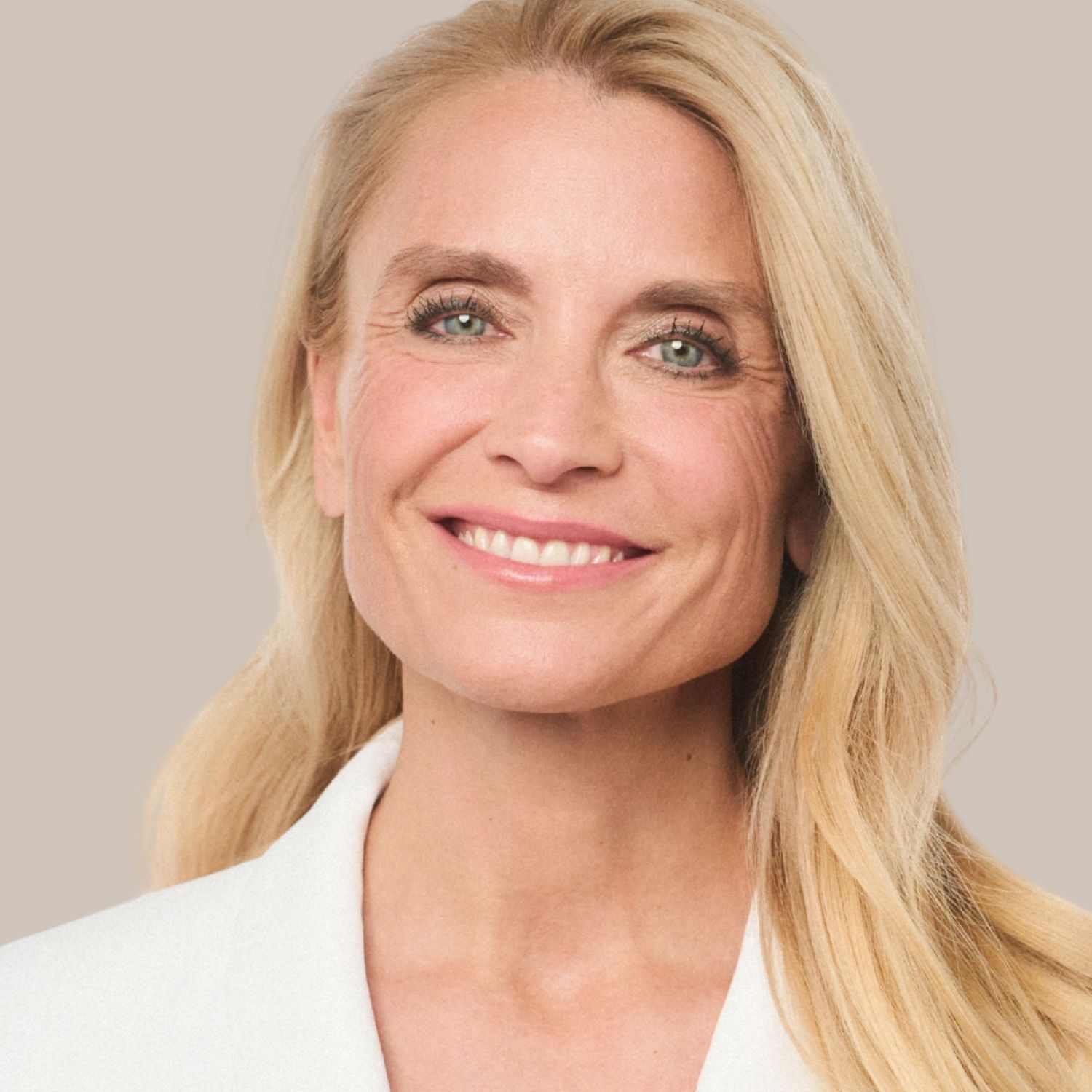 Porträt einer lächelnden blonden Frau mit langen Haaren, die eine weiße Jacke trägt.