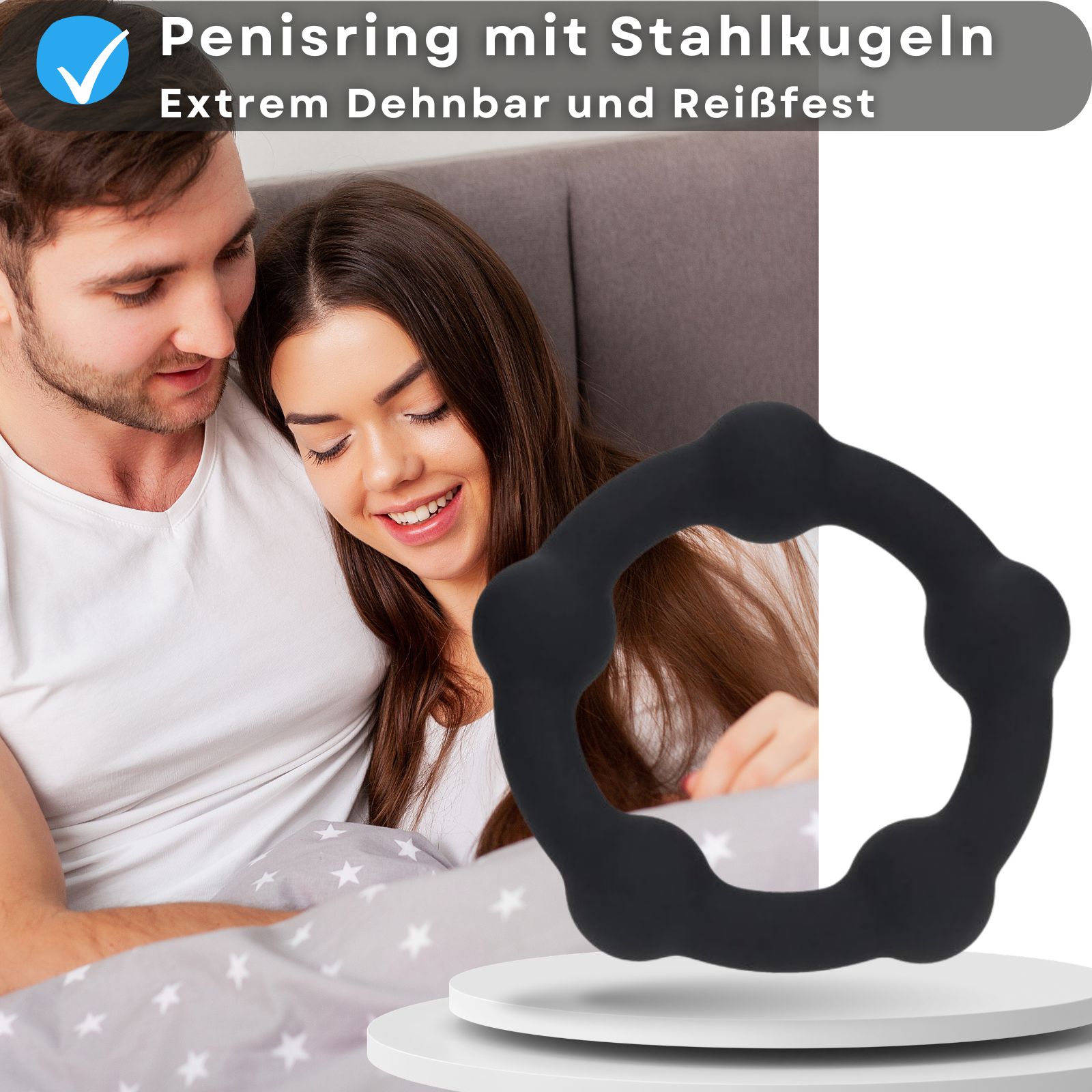 Ein schwarzer Penisring mit Stahlkugeln. Paar im Hintergrund. Aufschrift: Penisring mit Stahlkugeln, dehnbar.