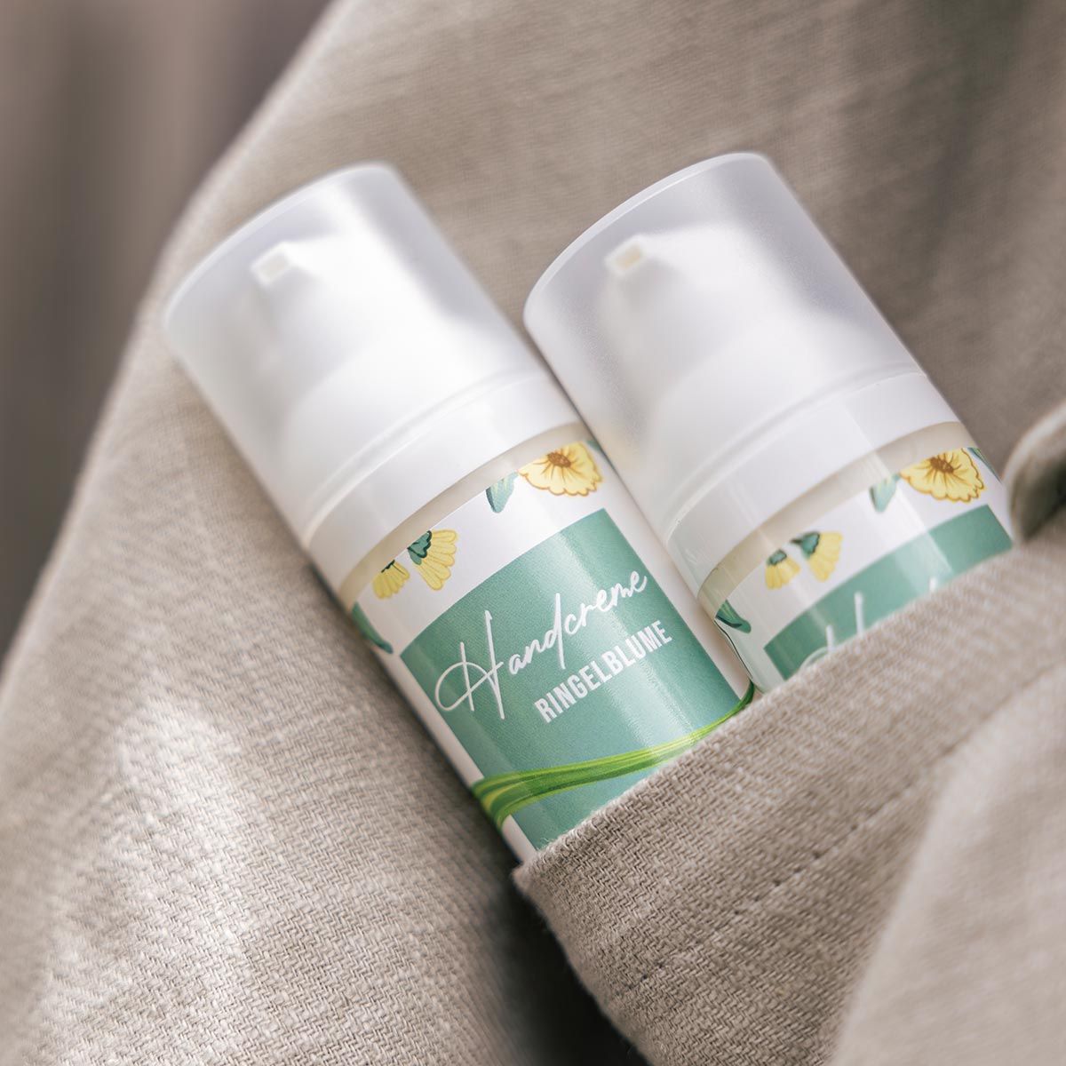 Zwei Handcreme-Spender mit floralem Etikett. Aufschrift: Handcreme Ringelblume, Karo Natura. In einer Stofftasche.