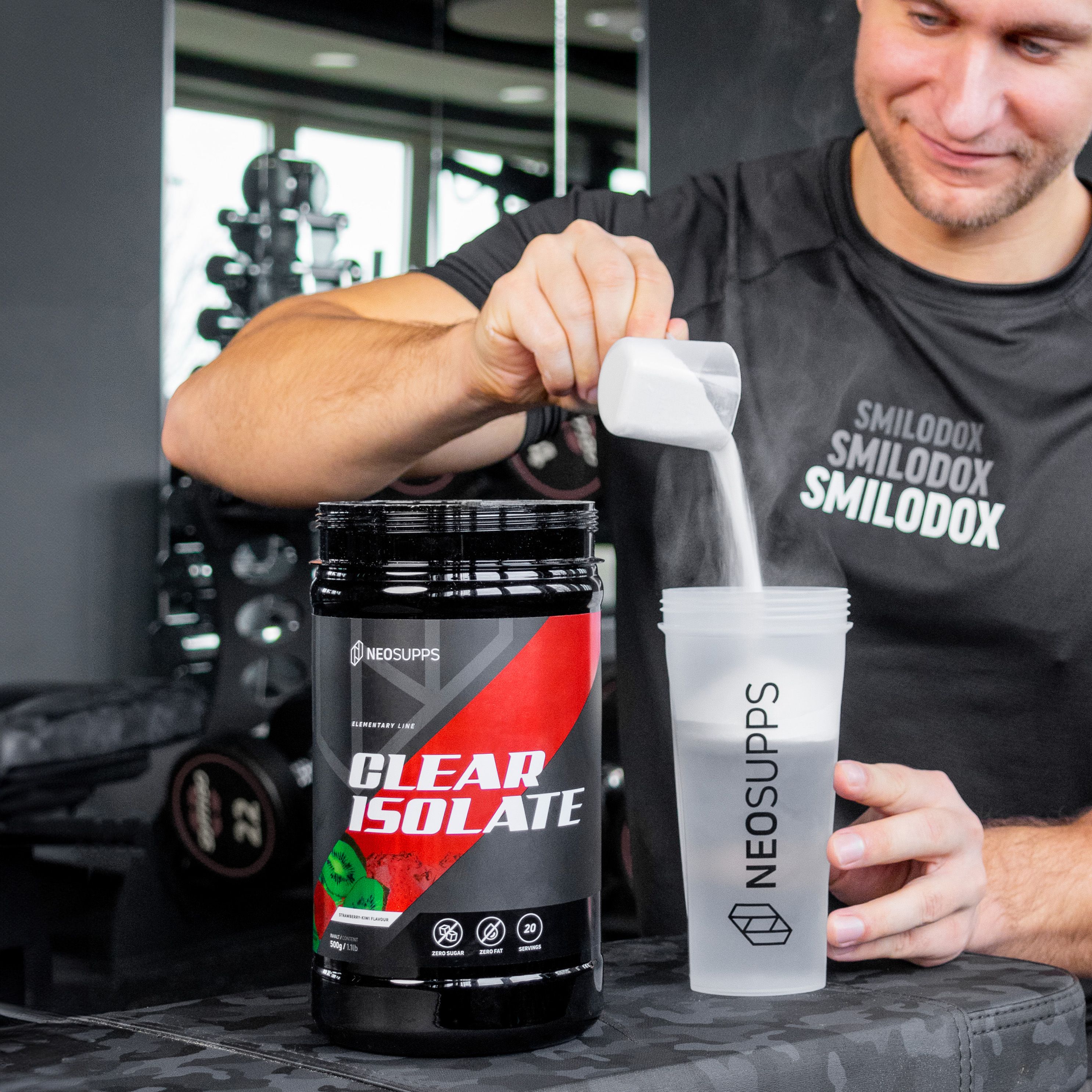 Mann gießt Pulver in Shaker. Schwarze Dose mit rotem Akzent. Aufschrift: CLEAR ISOLATE. Shaker mit Logo.