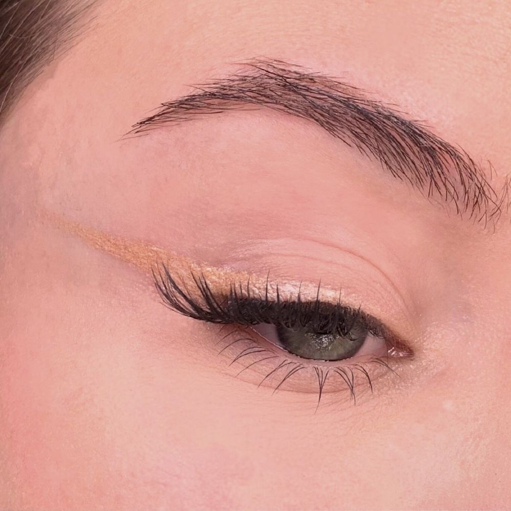 Auge mit Eyeliner. Beige Eyeliner auf dem Augenlid. Wimpern und Augenbraue sichtbar.