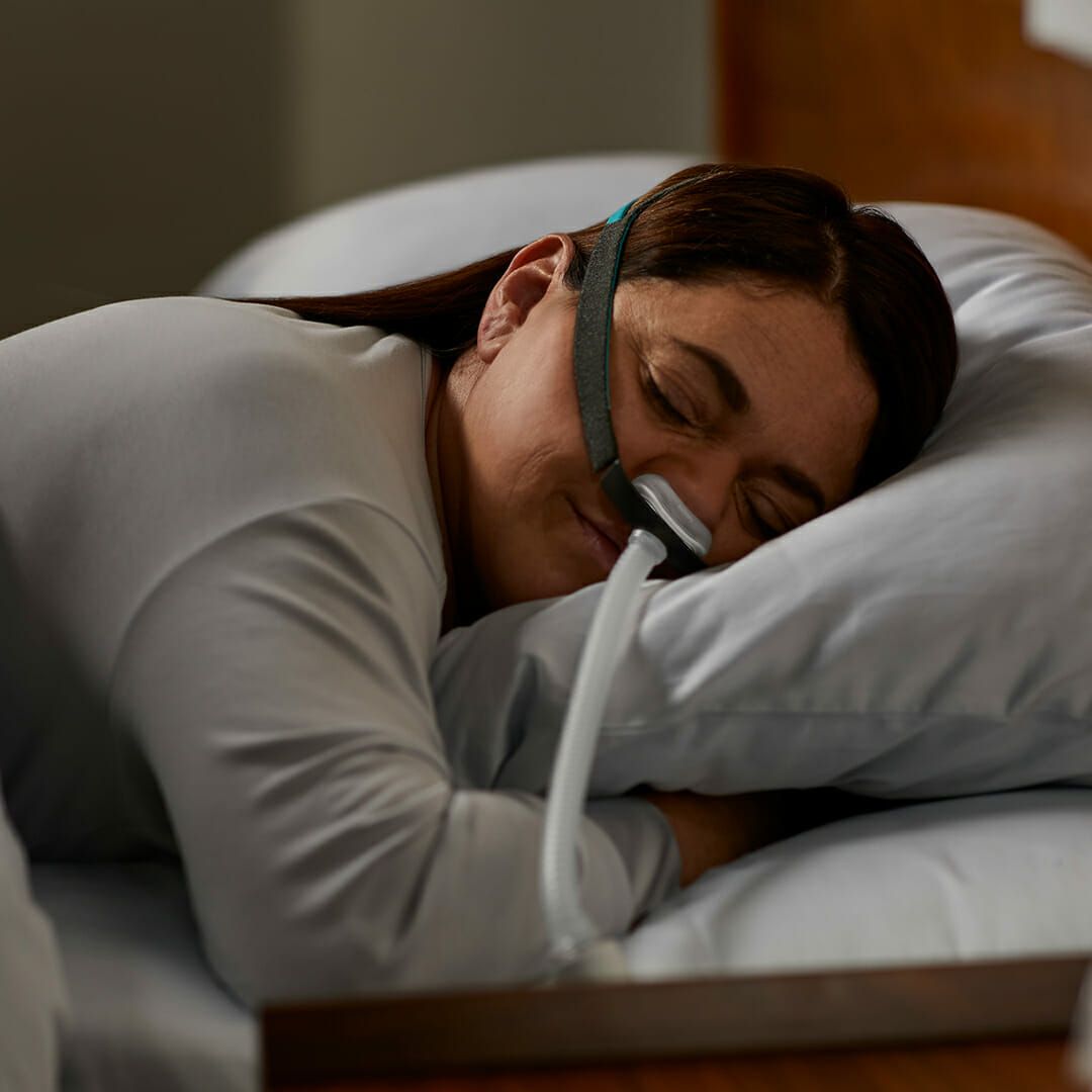 Frau schläft mit CPAP-Nasenmaske auf dem Kissen.