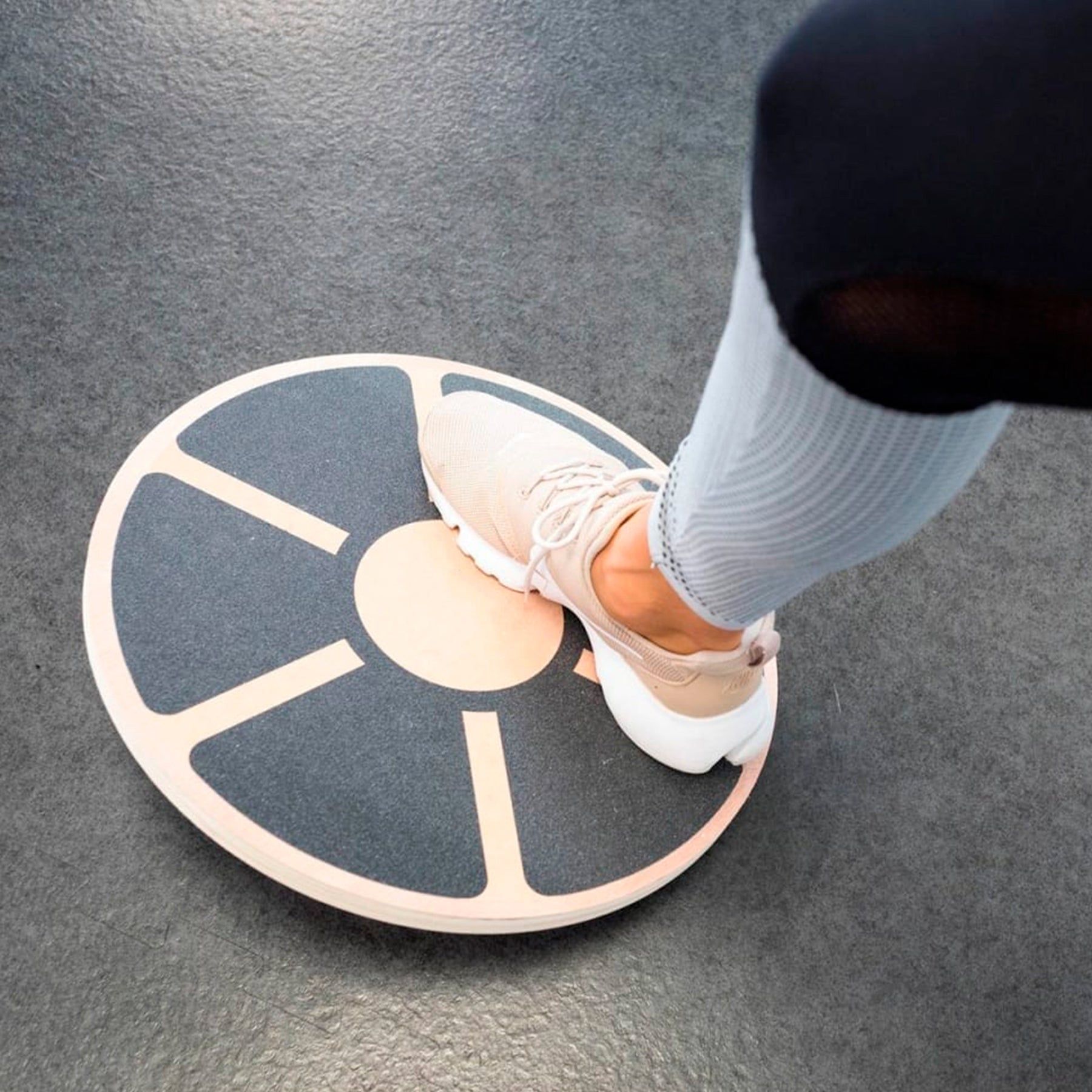 Balanceboard mit Fuß. Schwarze, rutschfeste Oberfläche mit hellen Holzstreifen. Fuß auf dem Board.