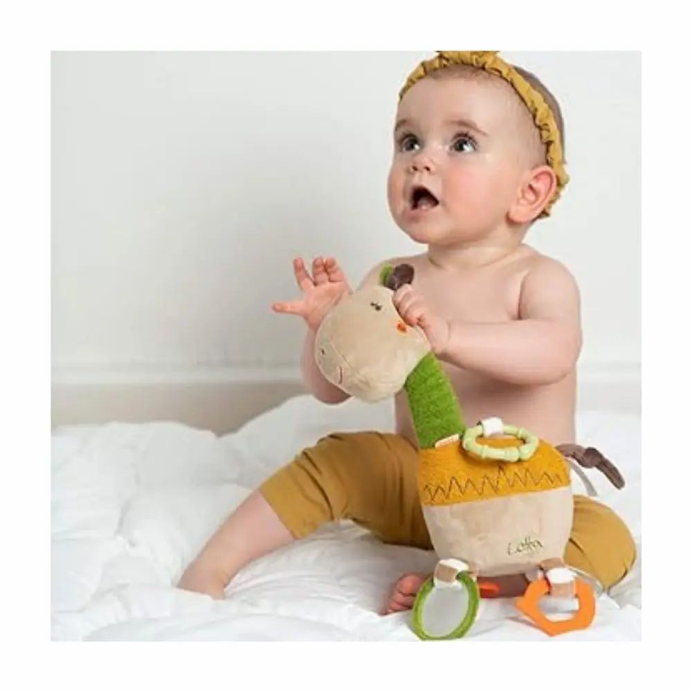 Baby hält Kuscheltier-Giraffe. Beige, grün und gelb. Mit Ringen und Spiegeln. Aufschrift "Lotta". Baby trägt Stirnband.