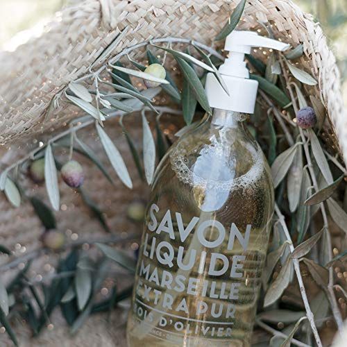 Flüssigseife in einer transparenten Flasche mit Pumpe, umgeben von Olivenzweigen. Aufschrift: Savon Liquide Marseille Extra Pur.