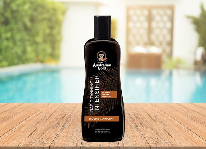 Braune Flasche auf Holzoberfläche. Aufschrift: Australian Gold, Rapid Tanning Intensifier, Biosine Complex. Hintergrund: Pool.