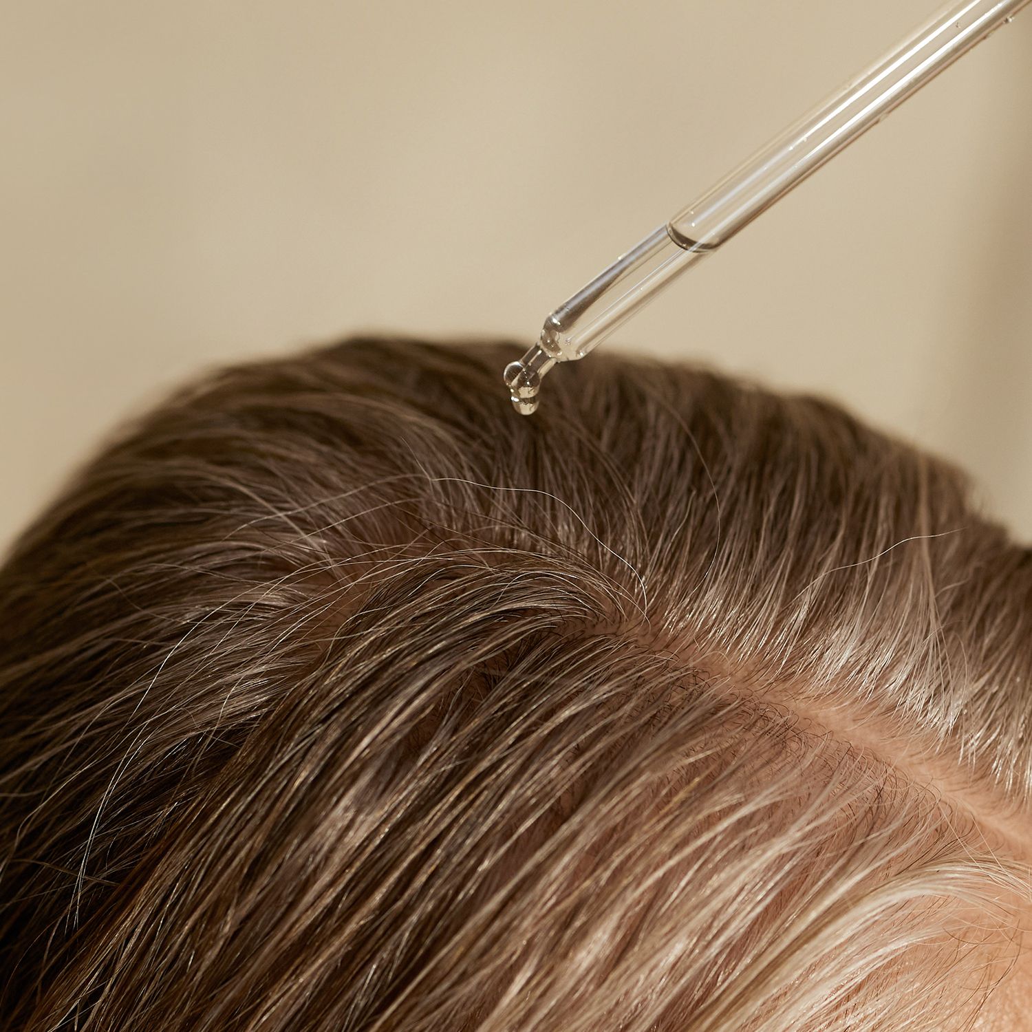 Tropfen Flüssigkeit auf Kopfhaut. Haare mit grauen Strähnen. Tropfer im Bild.