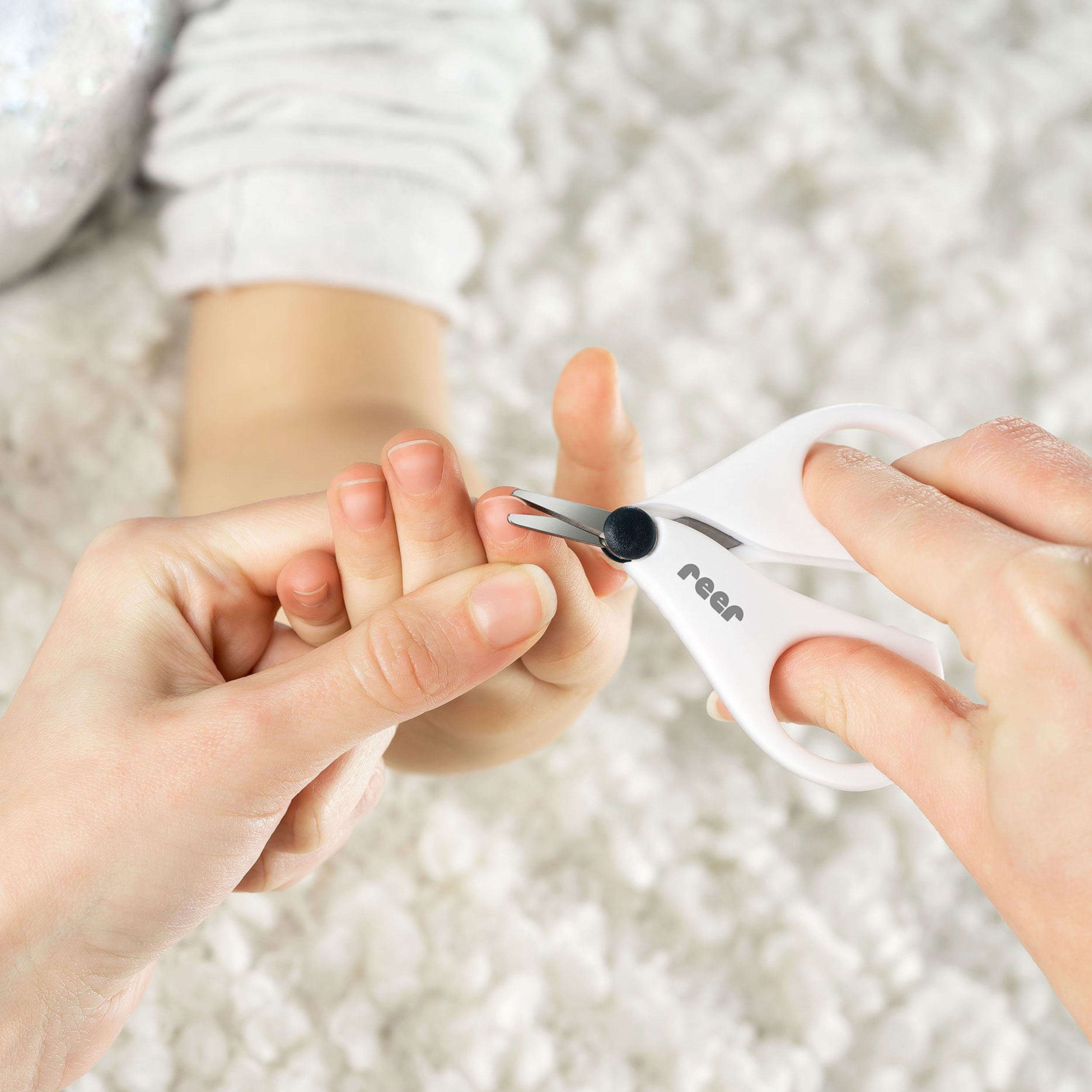 Weiße Nagelschere schneidet Fingernagel eines Babys. Marke: reer.
