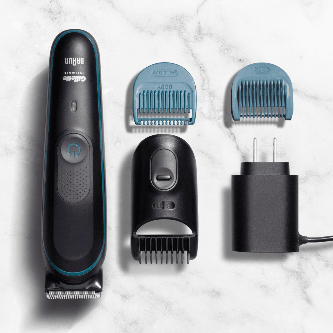 Schwarzer Trimmer mit blauen und schwarzen Aufsätzen und Ladegerät. Text: Gillette Intimate. Braun.