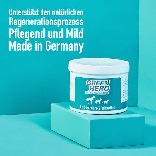 Weißer Tiegel mit blauem Etikett, auf blauem Podest. Aufschrift: GREEN HERO, Lebertran-Zinksalbe. Made in Germany.