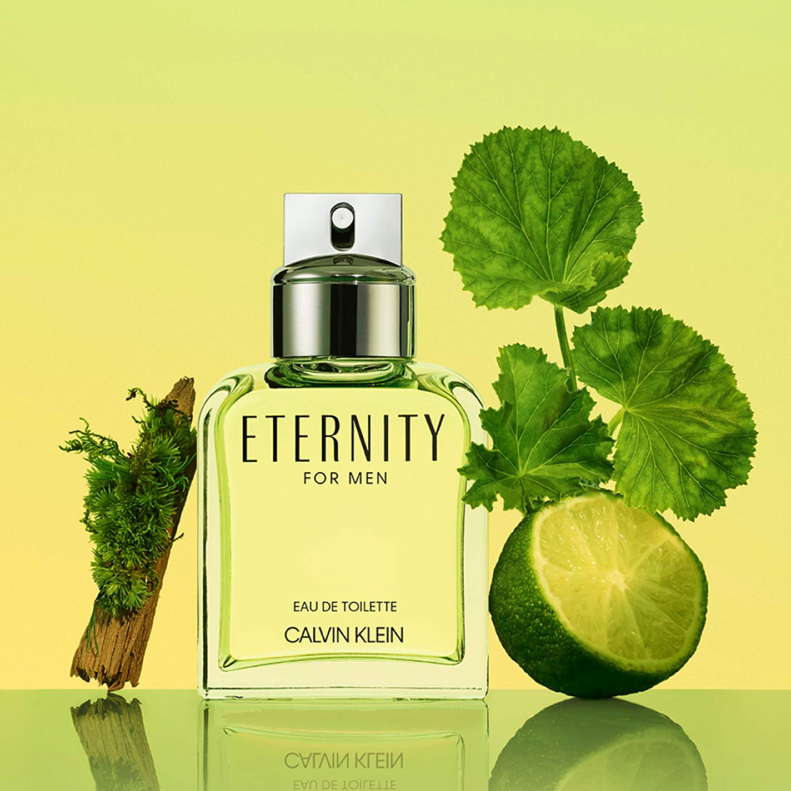 Eine rechteckige Glasflasche mit silbernem Verschluss, umgeben von grünen Blättern, Holz und einer Limettenscheibe. Auf der Flasche steht "ETERNITY FOR MEN".