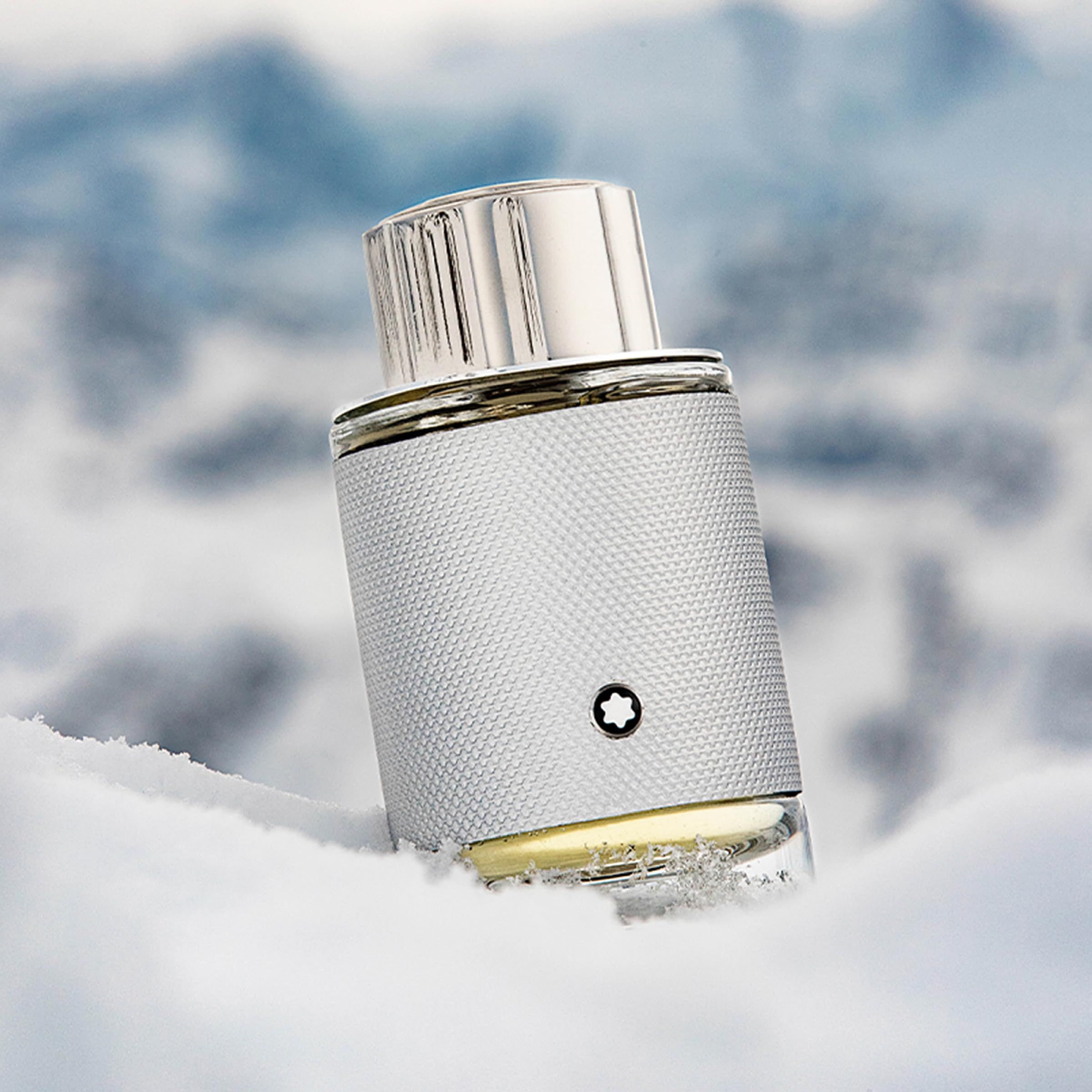 Montblanc Explorer Platinum EdP Nat. Spray. Silberner Flakon im Schnee. Silberne Kappe und Flakon mit Logo. Hintergrund: verschneite Berge.