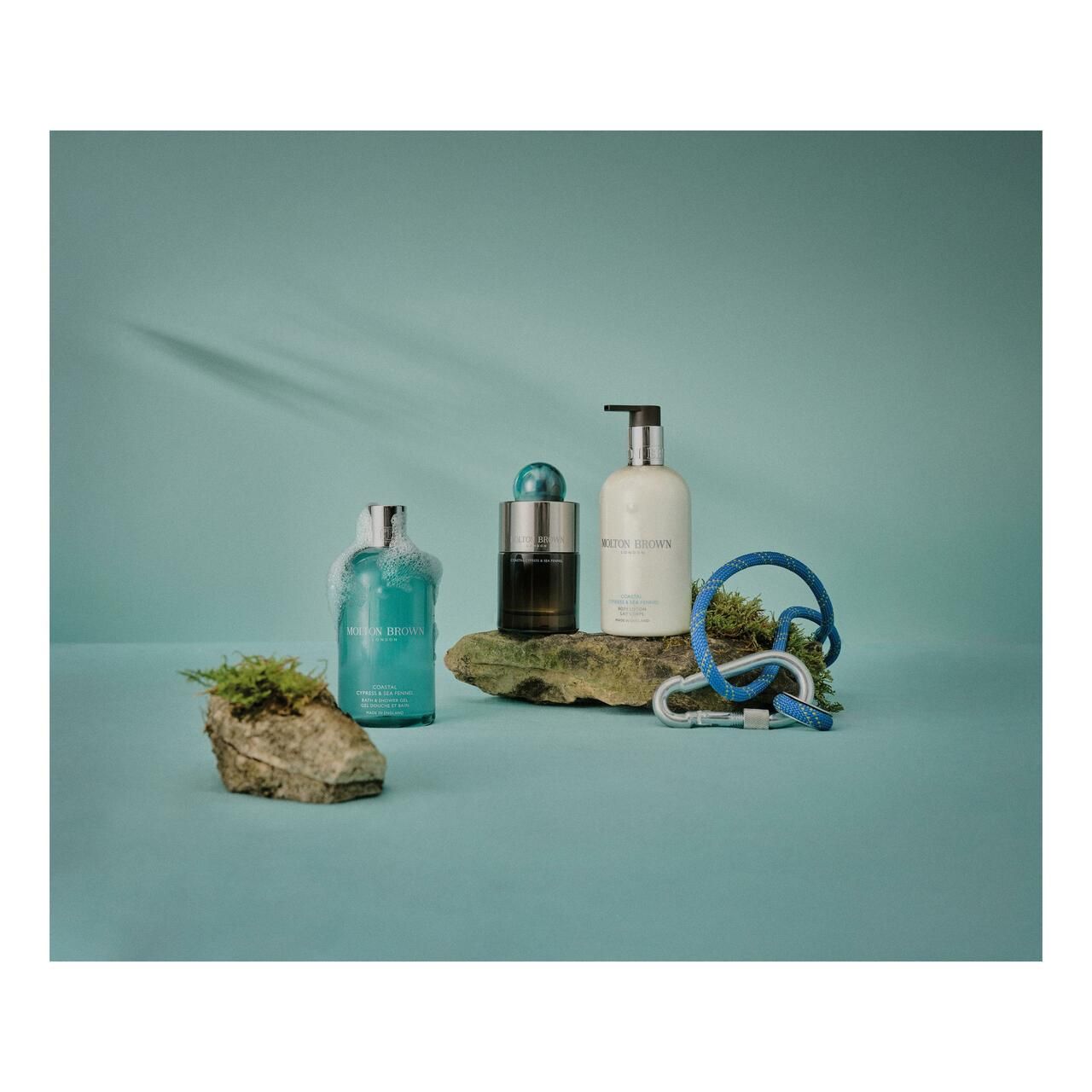 Drei Flaschen auf Steinen, blaue Oberfläche. Eine Flasche Shampoo, eine mit schwarzem Inhalt, eine mit Pumpe. Blaue Kletterausrüstung.