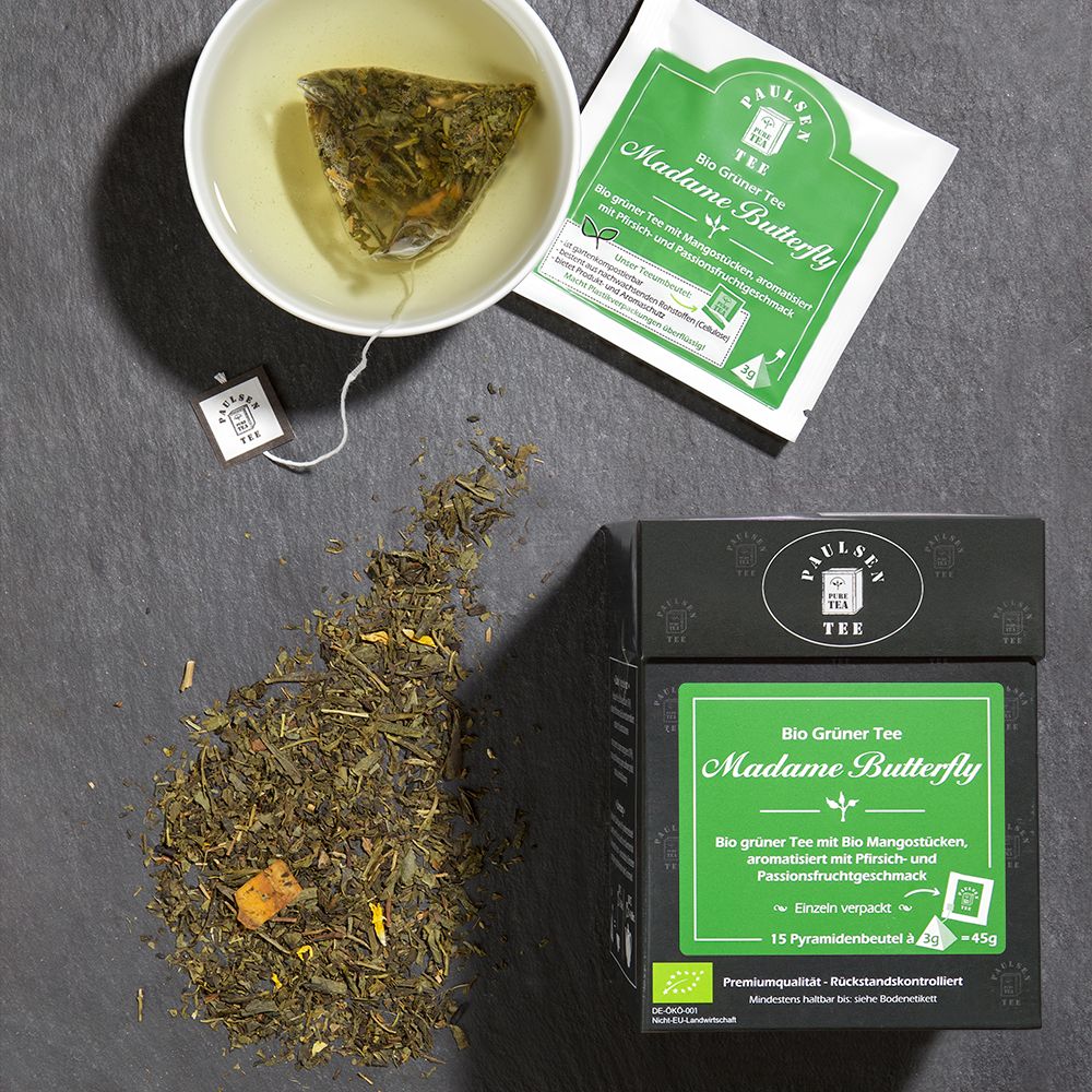 Tasse Tee, Teebeutel und Box "Madame Butterfly". Grüner Tee mit Mangostücken. Verpackung mit Logo "Paulsen Tee".