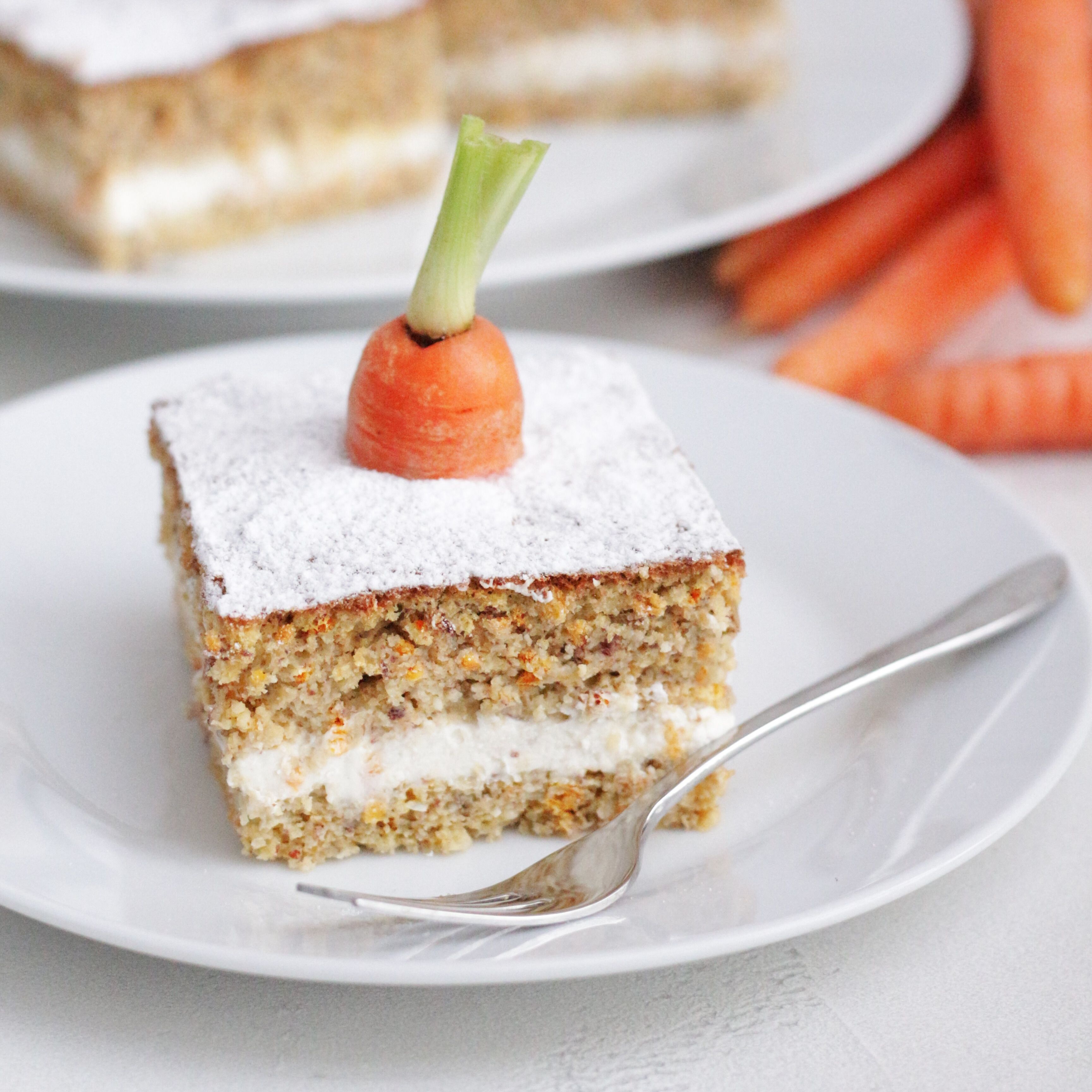 Kuchenstück auf Teller, Karottenstück als Dekoration. Puderzucker. Gabel.