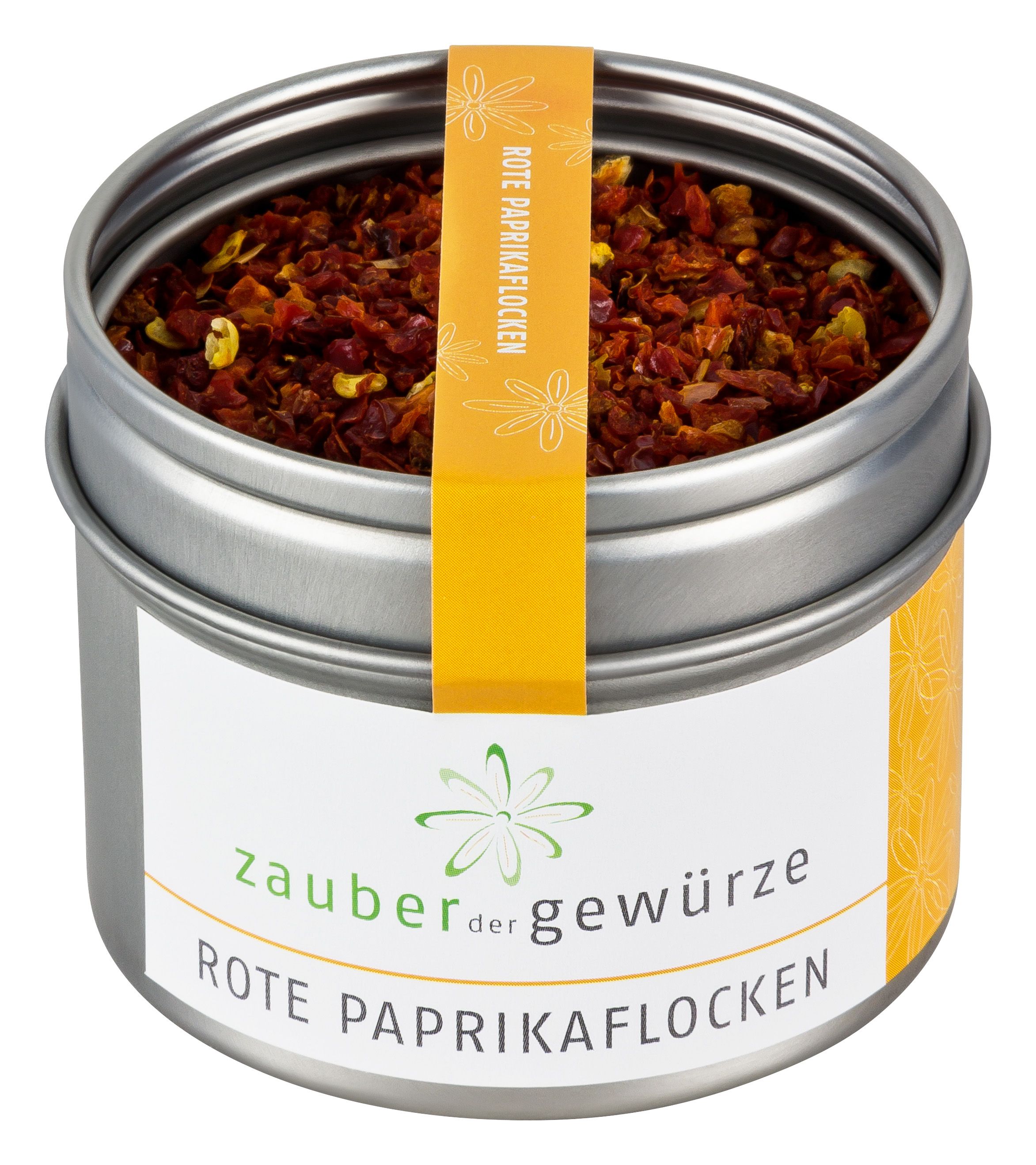 Metallbehälter mit roten Paprikaflocken. Gelbes Etikett mit Text: Zauber der Gewürze Rote Paprikaflocken.