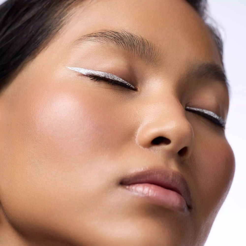 Nahaufnahme eines Gesichts mit geschlossenen Augen. Silberner Eyeliner-Strich am oberen Lid.