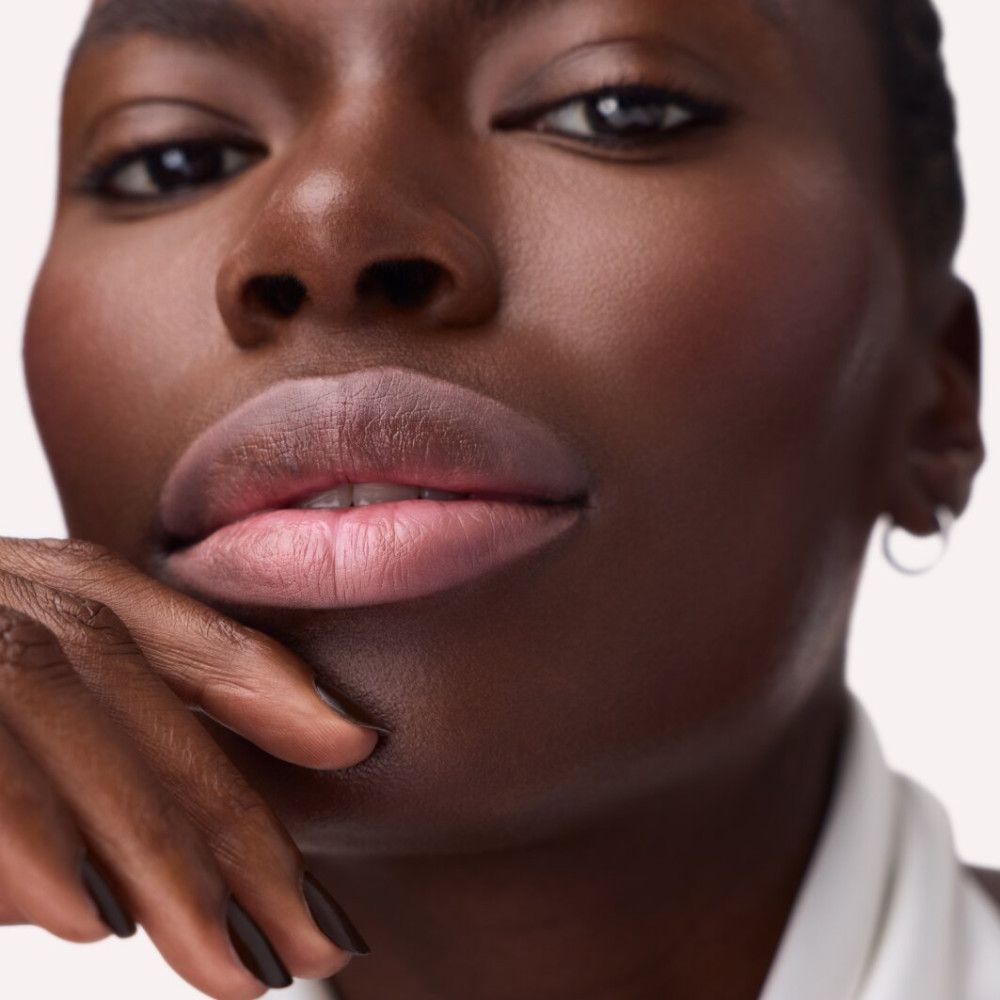 Nahaufnahme von Lippen, die mit einem rosa Lippenkonturenstift umrandet sind. Dunkle Hautfarbe.