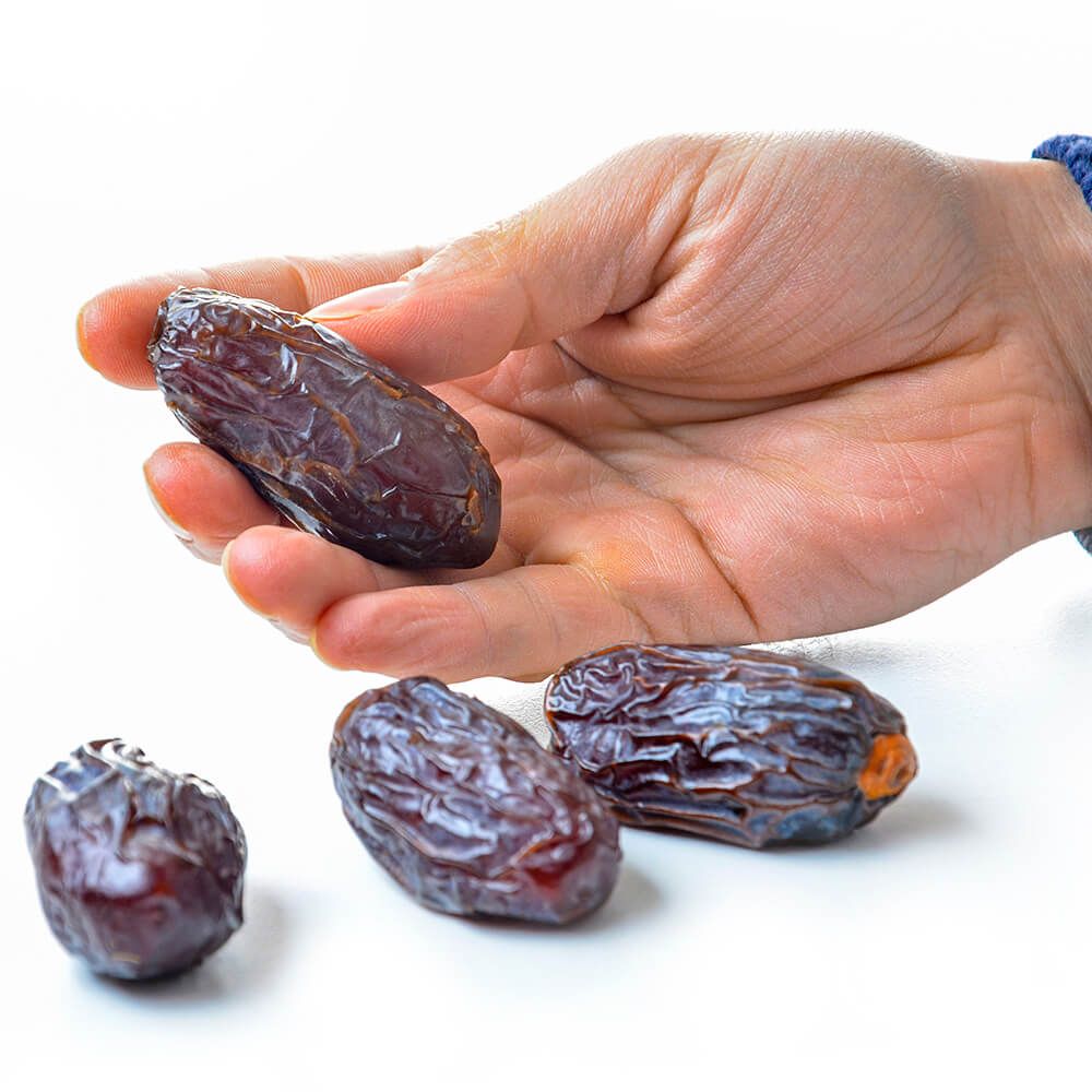 Hand hält mehrere Medjool-Datteln. Einzelne Datteln auf weißem Hintergrund.