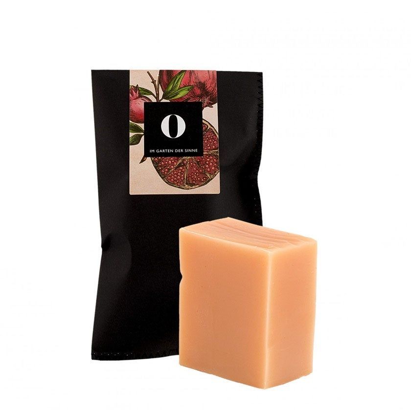 Rechteckige Seife neben schwarzer Verpackung mit Logo und Granatapfel-Illustration. Seife in hellem Rosa.