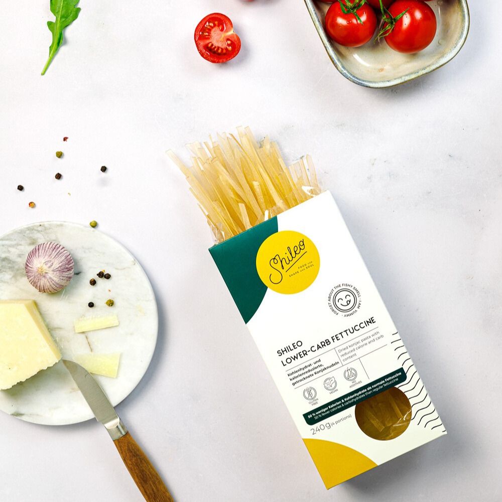 Packung SHILEO Lower-Carb Fettuccine. Daneben Tomaten, Käse, Knoblauch und eine Gabel. Aufschrift: 240g.