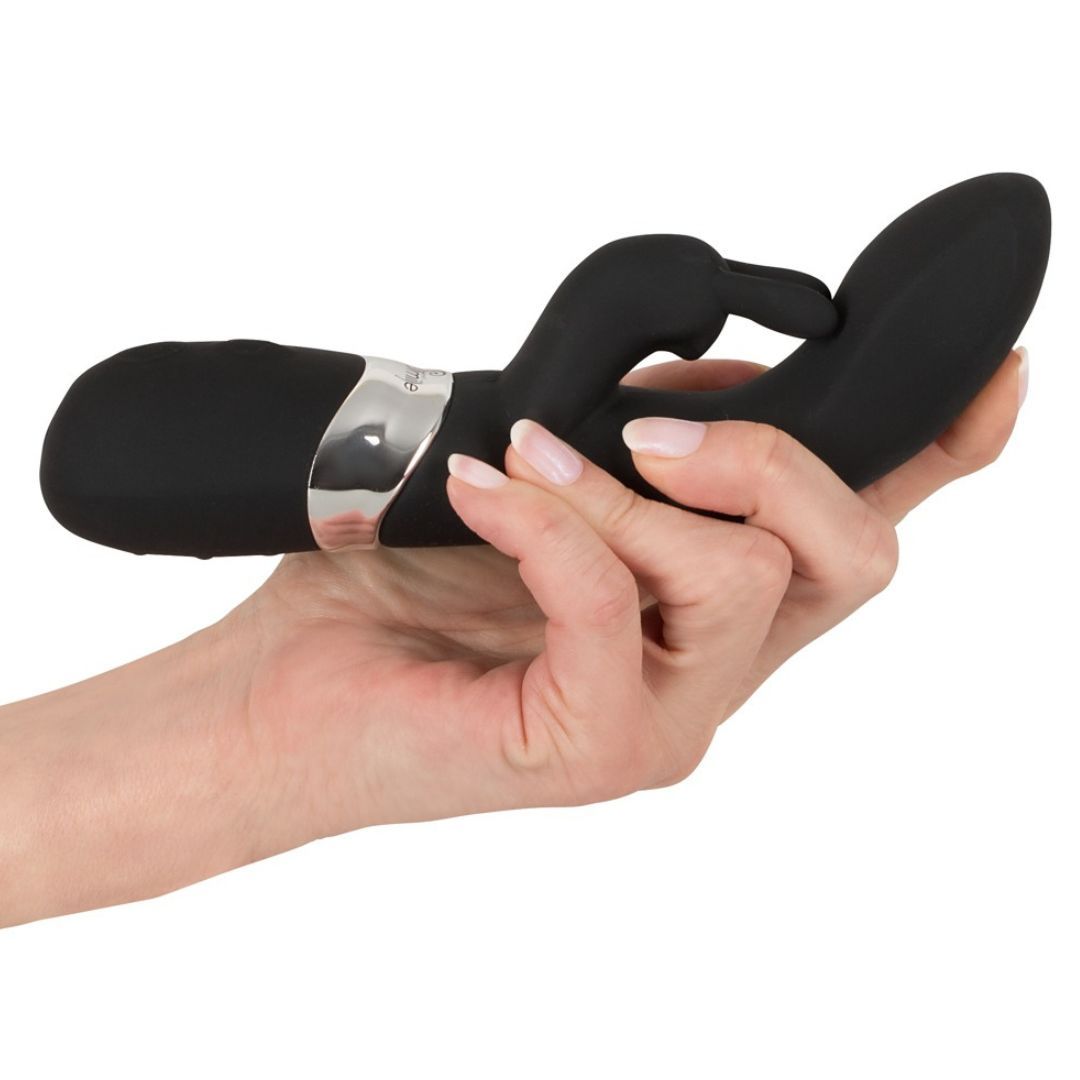Schwarzer Vibrator mit flexiblen Öhrchen, in einer Hand gehalten. Silbernes Band.
