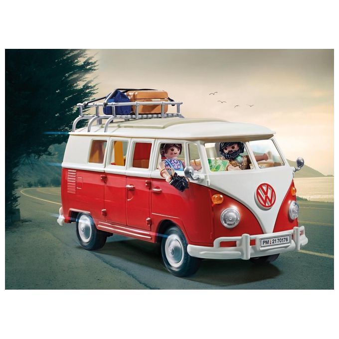 Un furgone giocattolo VW rosso e bianco Playmobil. Sul tetto ci sono bagagli e un portapacchi. All'interno ci sono due personaggi Playmobil. Il veicolo viaggia su una strada con un paesaggio costiero sullo sfondo.