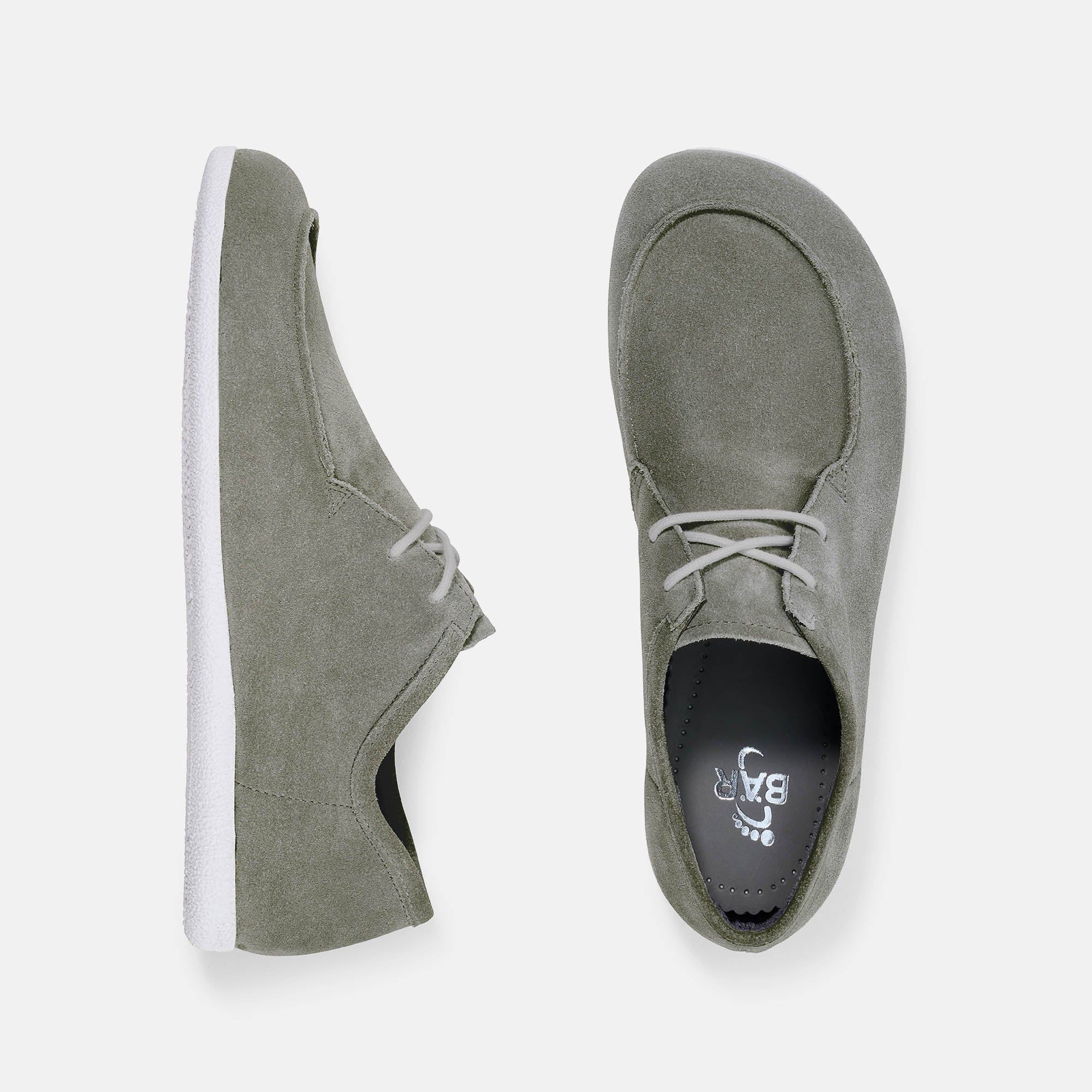 Zwei graue Schnürschuhe mit weißer Sohle. Wildleder-Obermaterial. Breite Passform. Blick von oben auf die Schuhe.