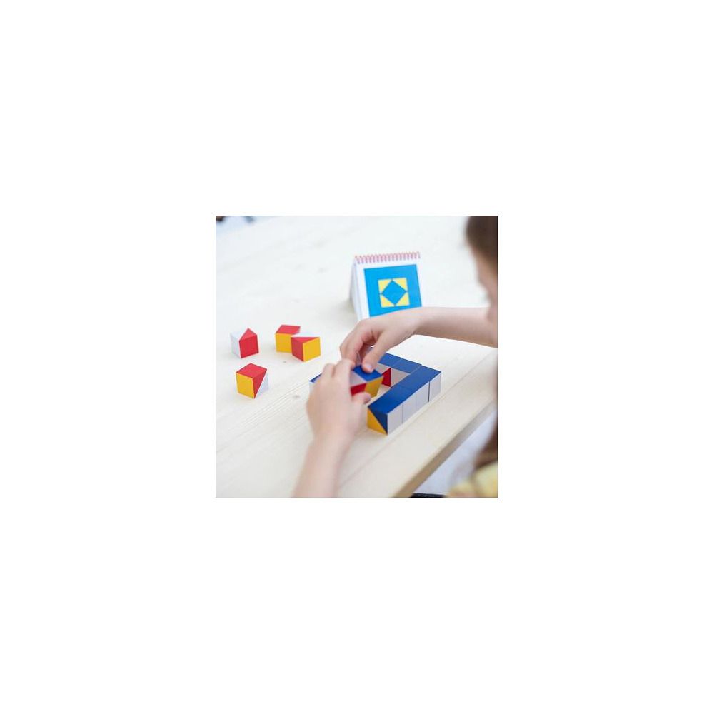 Kind spielt mit bunten Würfeln und einer Vorlagenkarte. Die Würfel sind teilweise zu einer Form zusammengesetzt.