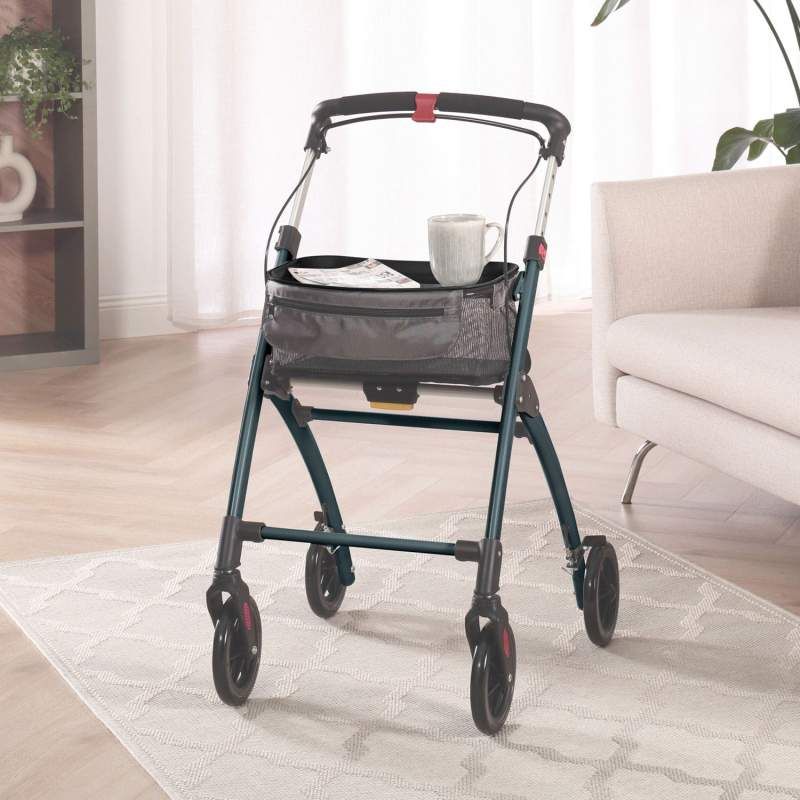 Rollator im Wohnzimmer. Korb mit Tasse und Papier. Blaues Gestell, vier Räder.