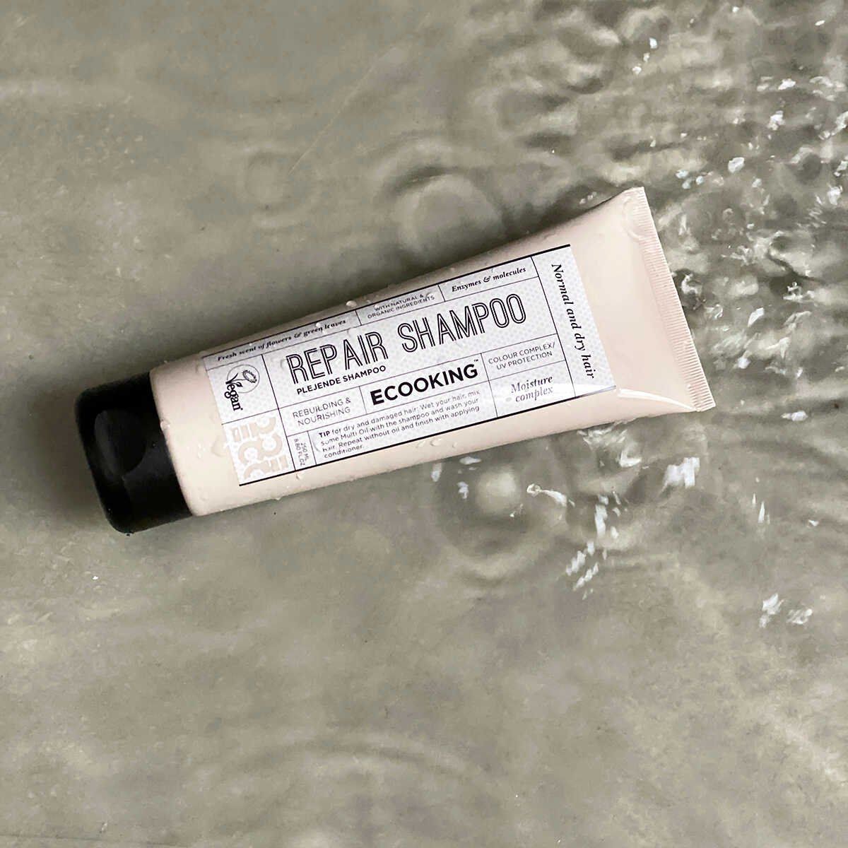 Beige Tube mit schwarzem Deckel im Wasser. Aufschrift: Repair Shampoo, Ecooking. Für normales und trockenes Haar. Vegan.