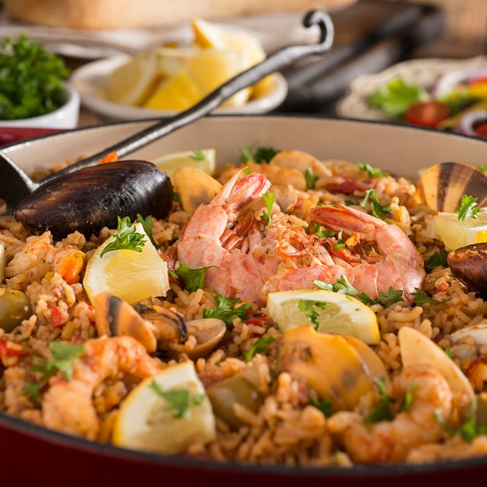 Paella mit Meeresfrüchten, Zitrone und Gemüse in einer roten Pfanne. Nahaufnahme.