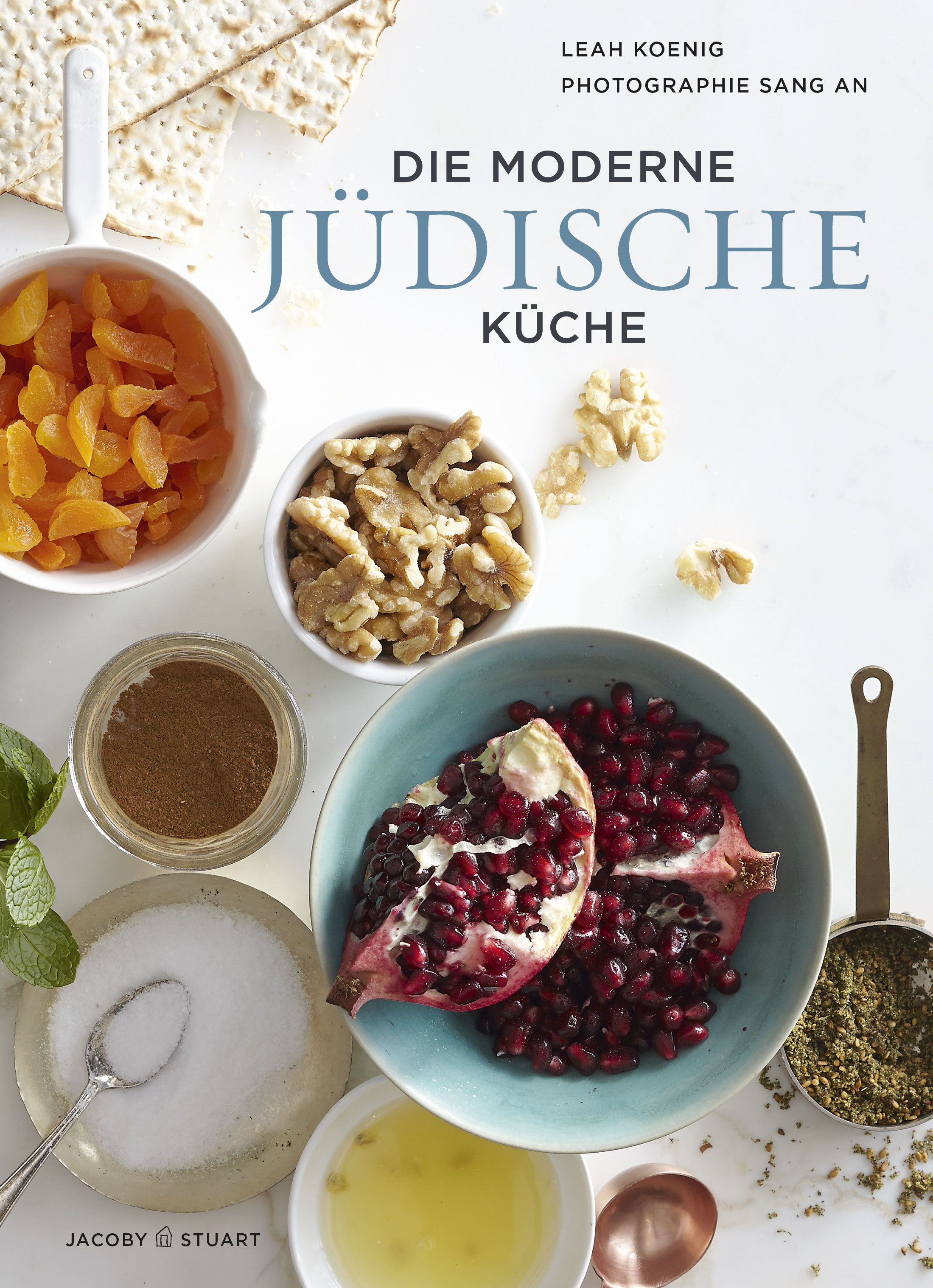 Buchcover mit dem Titel „Die moderne jüdische Küche“. Auf dem Tisch sind Zutaten wie Granatapfel, Nüsse und Gewürze angeordnet.