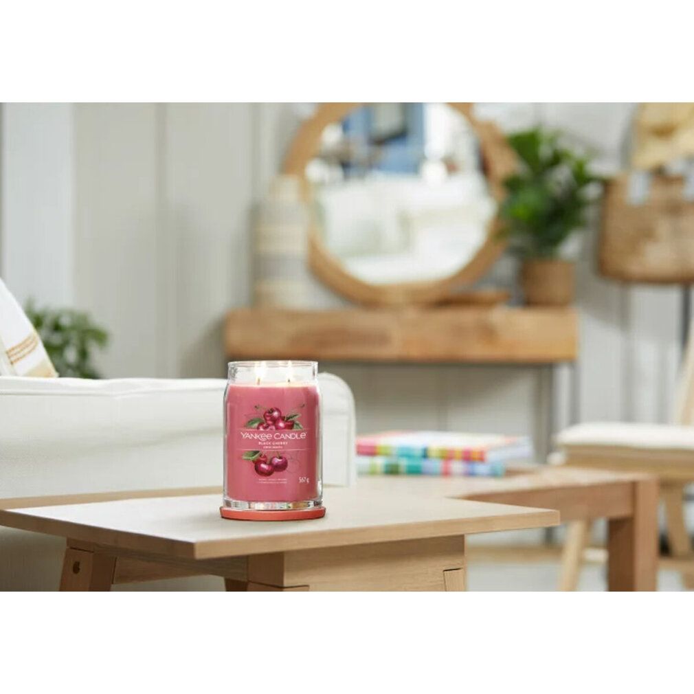 Yankee Candle Black Cherry auf einem Tisch. Rote Kerze in Glasbehälter mit zwei Dochten. Hintergrund unscharf.