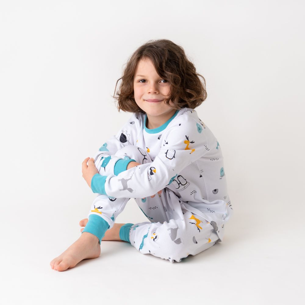 Kind trägt weißen Pyjama mit Tier-Motiven. Türkise Bündchen. Kind sitzt auf dem Boden.