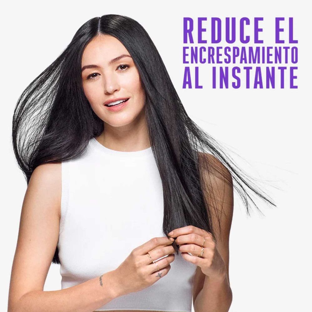 Frau mit langen, schwarzen Haaren. Text: Reduziert Frizz sofort. Sie hält ihre Haare in der Hand.