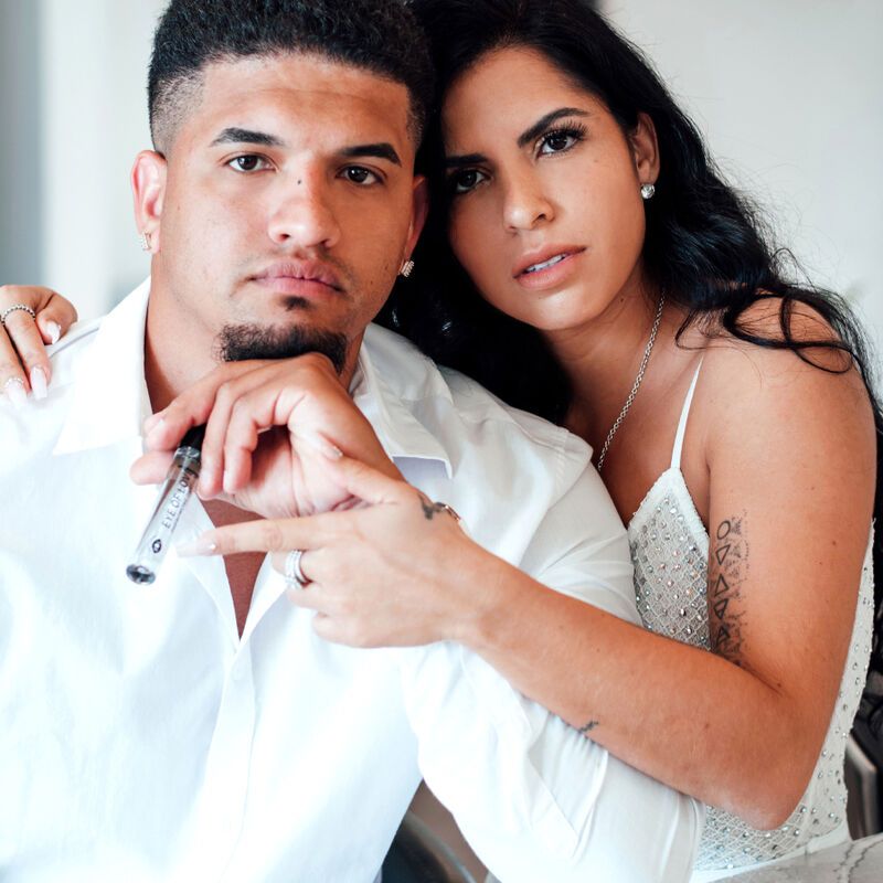 Ein Mann und eine Frau schauen in die Kamera. Der Mann hält eine Parfümflasche. Aufschrift: EYE OF LOVE Pheromone Parfum Romantic.