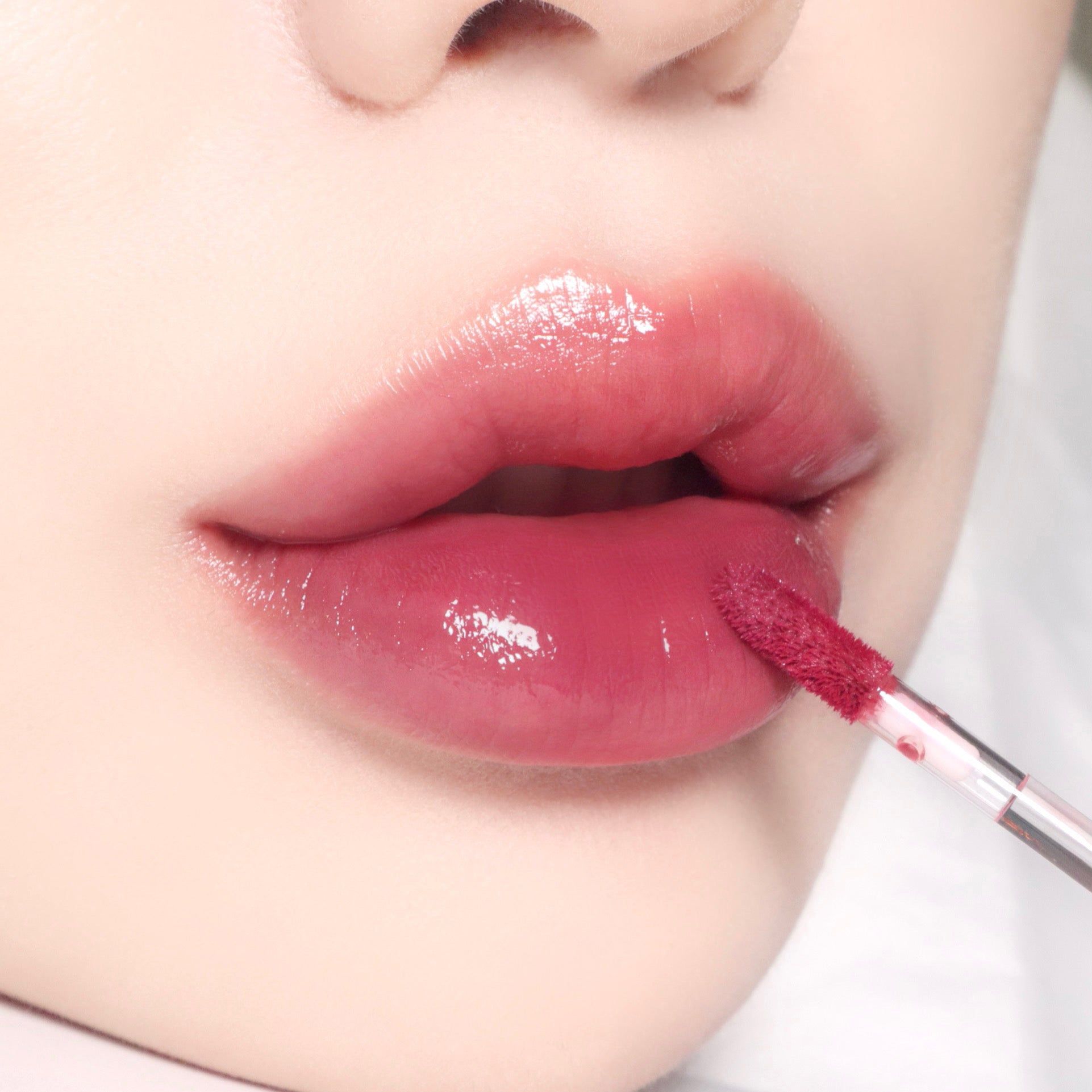 Nahaufnahme von Lippen mit rosafarbenem Lipgloss, der mit einem Applikator aufgetragen wird.